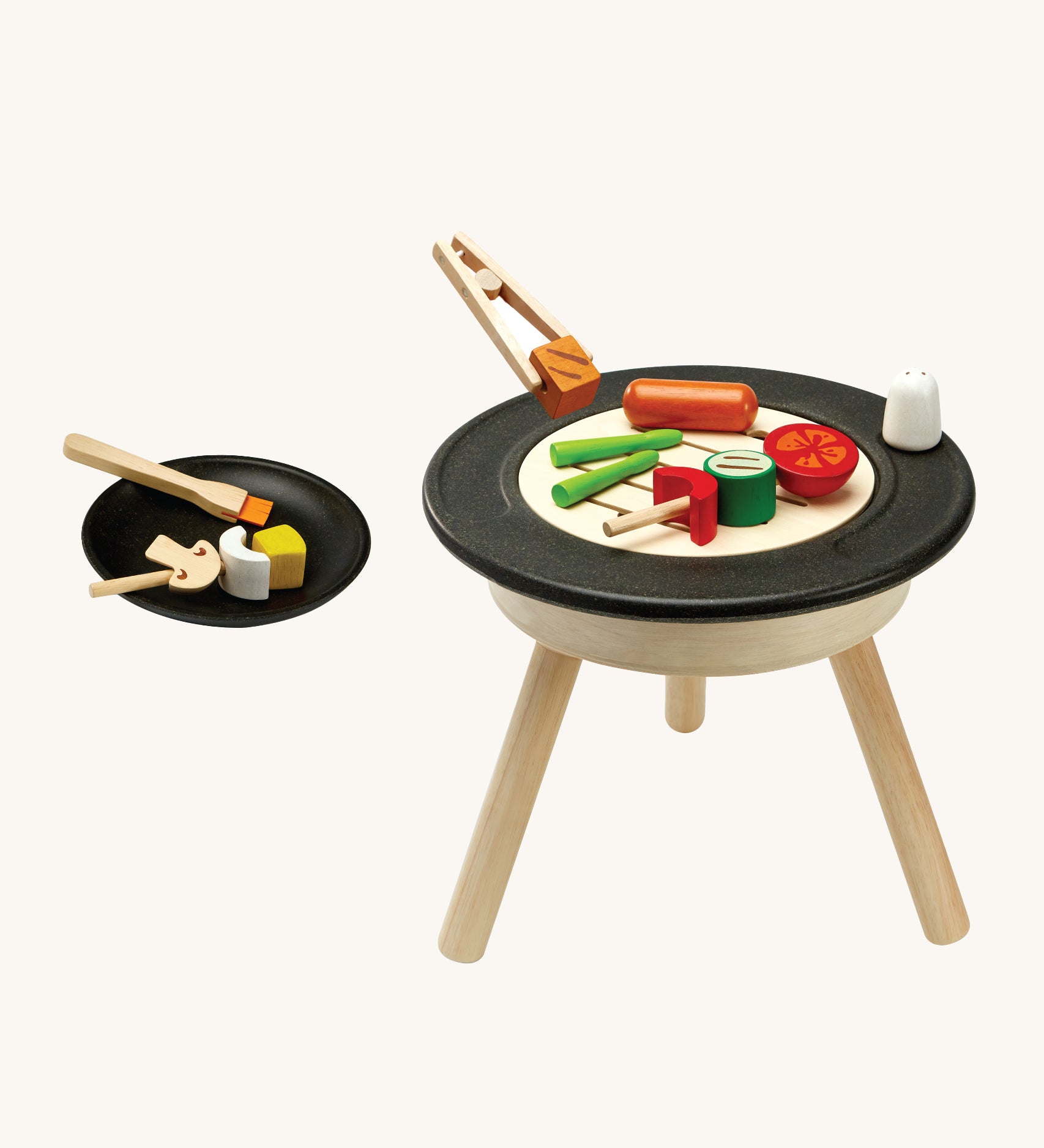 PlanToys kids wooden BBQ role play set which includes a selection of BBQ play food, skewers, basting brush, salt shaker, plate and a standing BBQ. The image is on a cream background