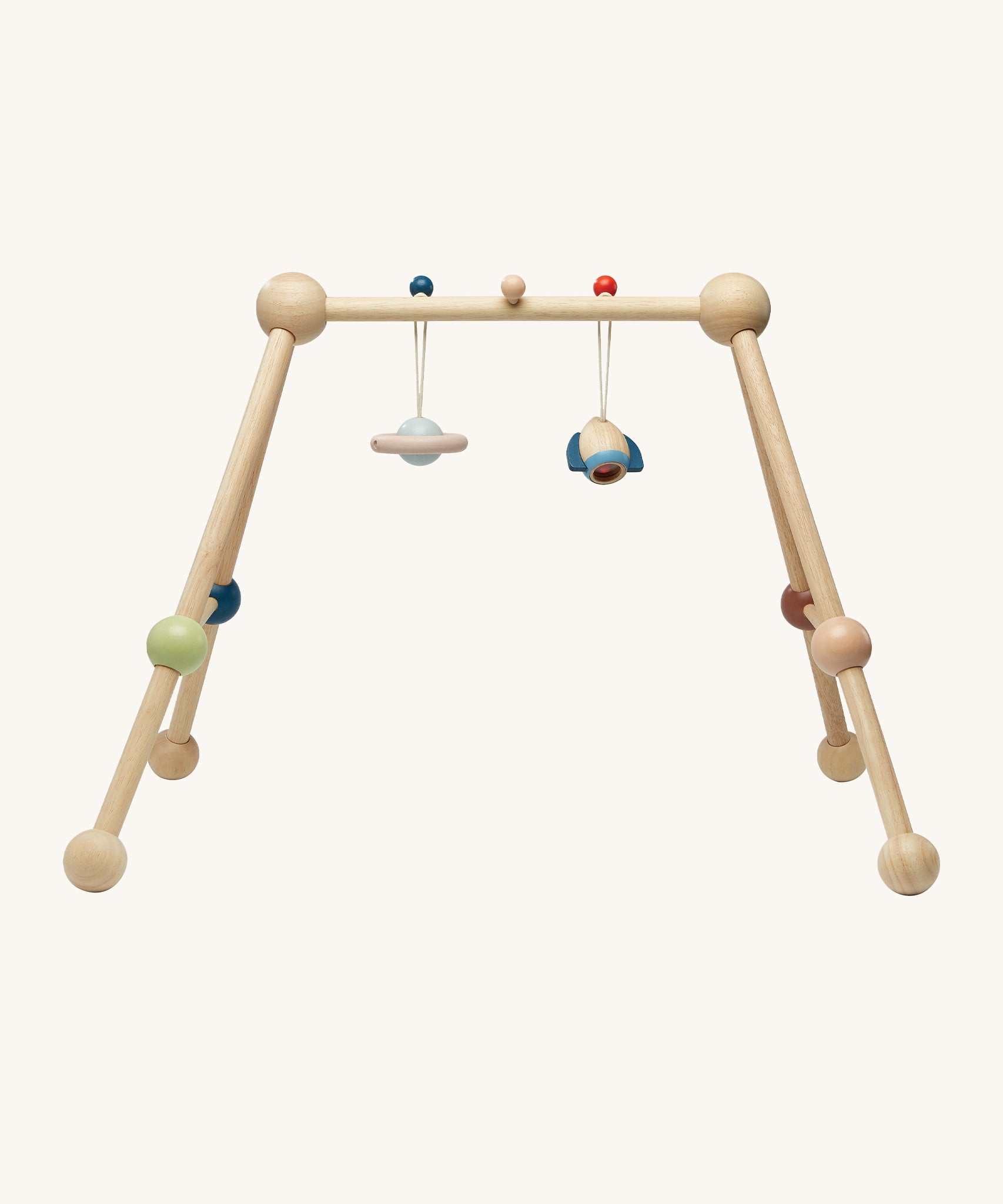 The PlanToys Play Gym in Orchard colours (natural wood, green, blue, brown and beige) with the rocket and planet sensory toys attached to the top using a blue and a red peg hook. This image is front on, on a cream background