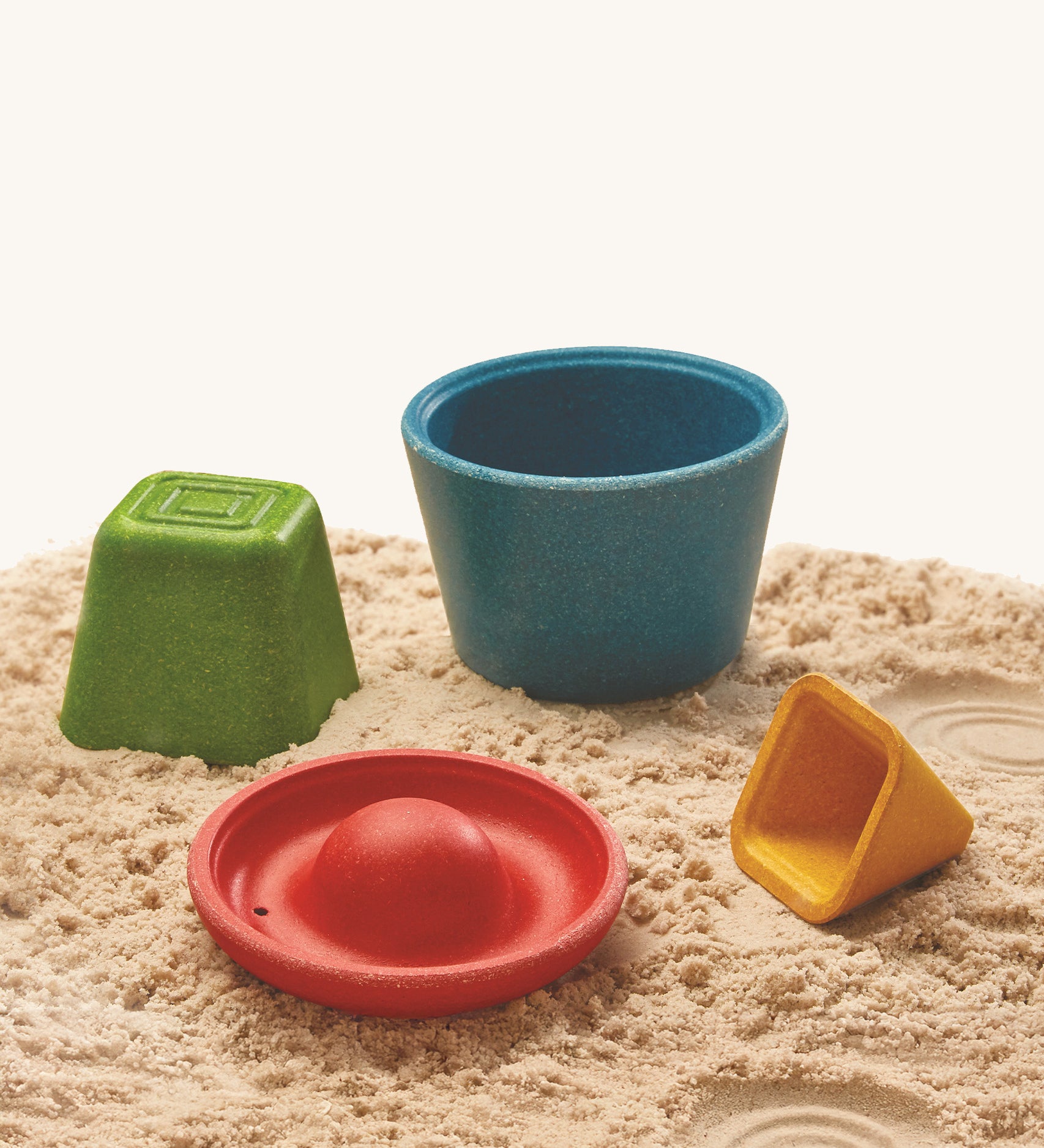 The PlanToys Creative Sand Play blocks are arranged on soft sand. Each block comes with a textured top for sensory play and to leave a textured print in the sand or mud