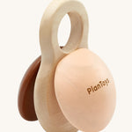 PlanToys Shake N Clap, wooden baby rattle toy offers a fun sensory experience for little ones. the clapper sides are in brown and beige, and the middle part is in natural wood with a hole in the top for easy gripping for little hands. The image is on a cream background