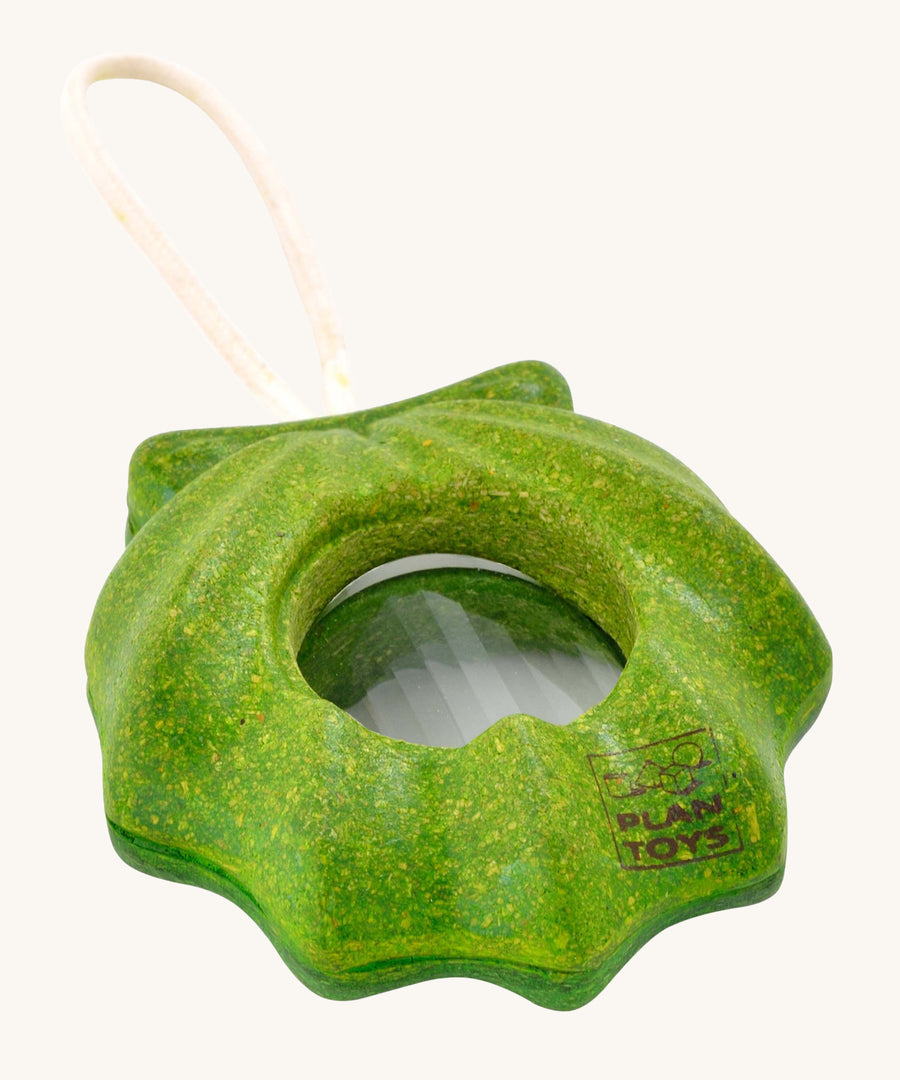 PlanToys Shell Kaleidoscope, is a green sensory kaleidoscope toy in the image of a shell, with a circular lens in the middle and a beige rope handle. The image is on a cream background 