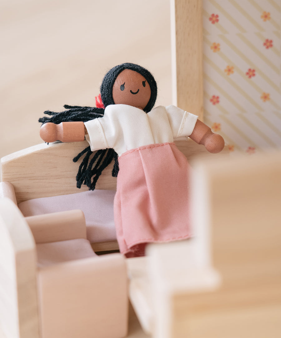 A doll shown sitting on the PlanToys Wooden sofa from the Living Room furniture set . 