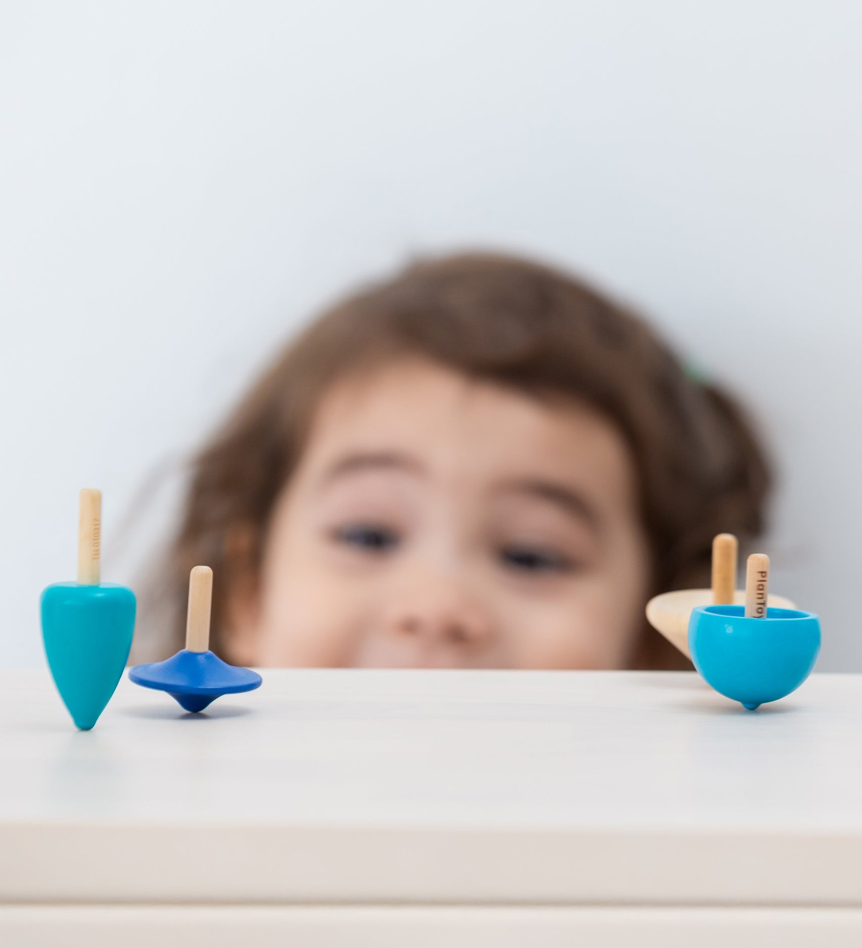 A child looking at the PlanToys Mini Spinning Tops whilst they are spinning on a wooden table top