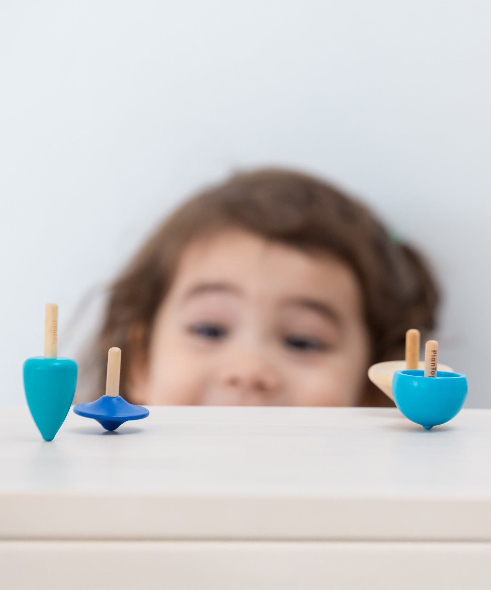 A child looking at the PlanToys Mini Spinning Tops whilst they are spinning on a wooden table top