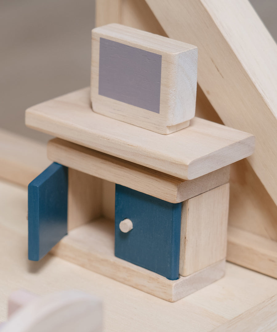 The TV and TV display unit from the PlanToys Living Room Dolls House Furniture Set shown in place in a wooden dolls house. 