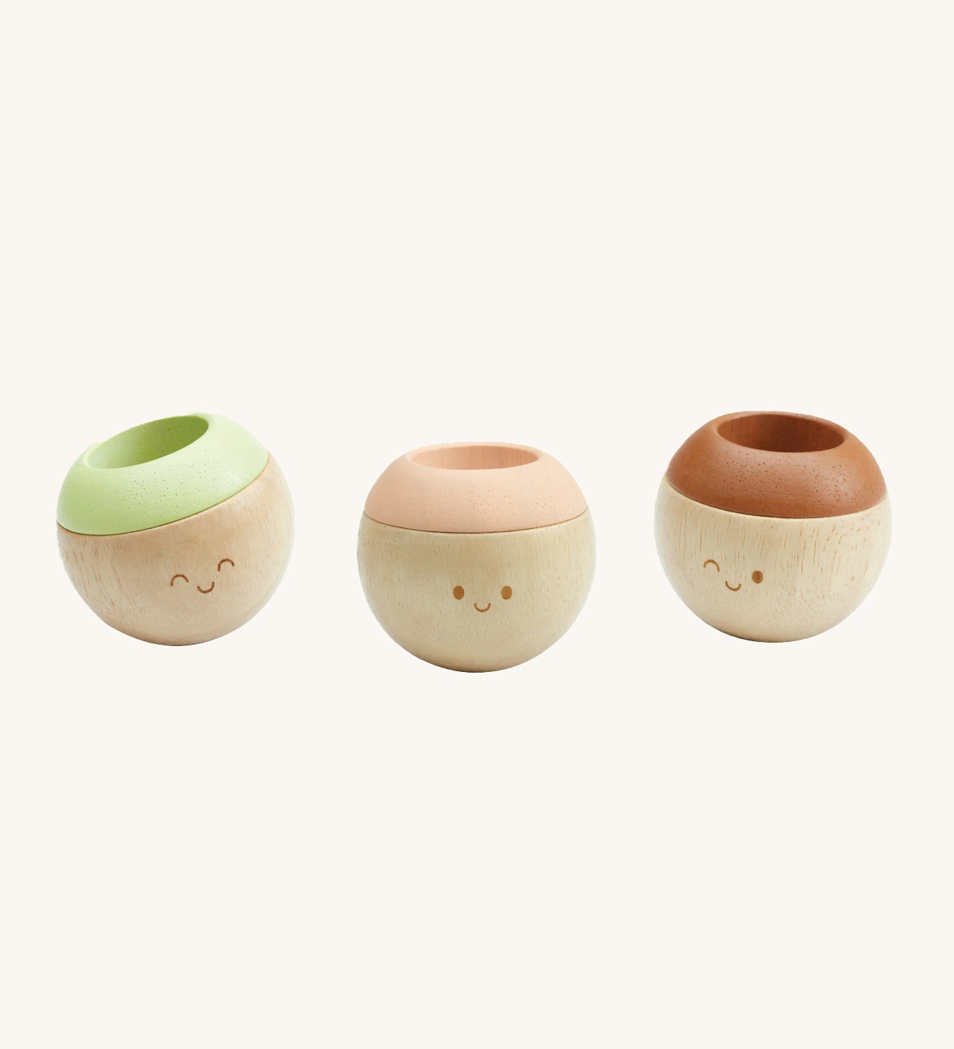 The PlanToys Sensory Tumblers - Modern Rustic, are three adorable round tumbling toys for little ones. each have a happy, smiling face. The one on the left has a green top, the middle has a pink top, and the right one has a brown top. The image is on a cream background