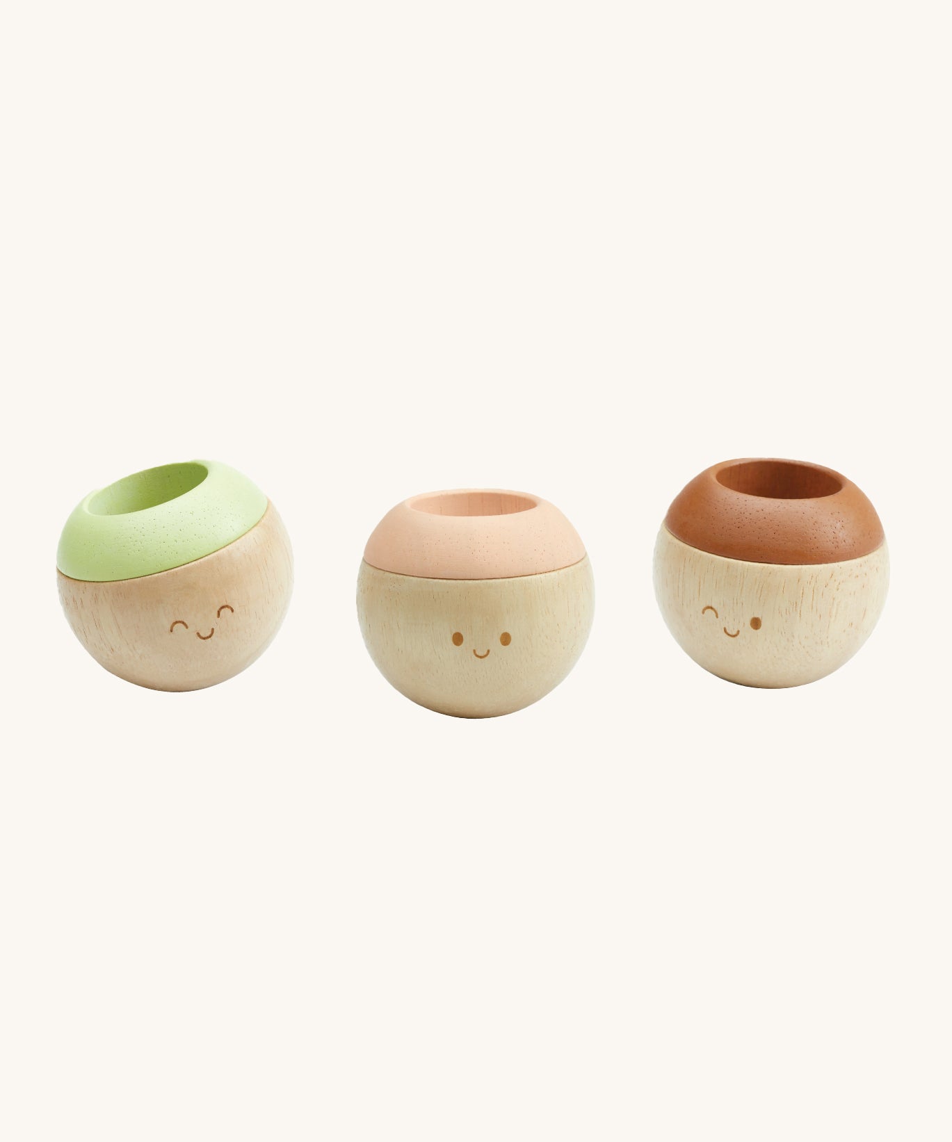 The PlanToys Sensory Tumblers - Modern Rustic, are three adorable round tumbling toys for little ones. each have a happy, smiling face. The one on the left has a green top, the middle has a pink top, and the right one has a brown top. The image is on a cream background