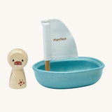 PlanToys children's wooden walrus peg doll figure is next to a blue wooden sailing boat bath toy with a white sail, and is on a cream background