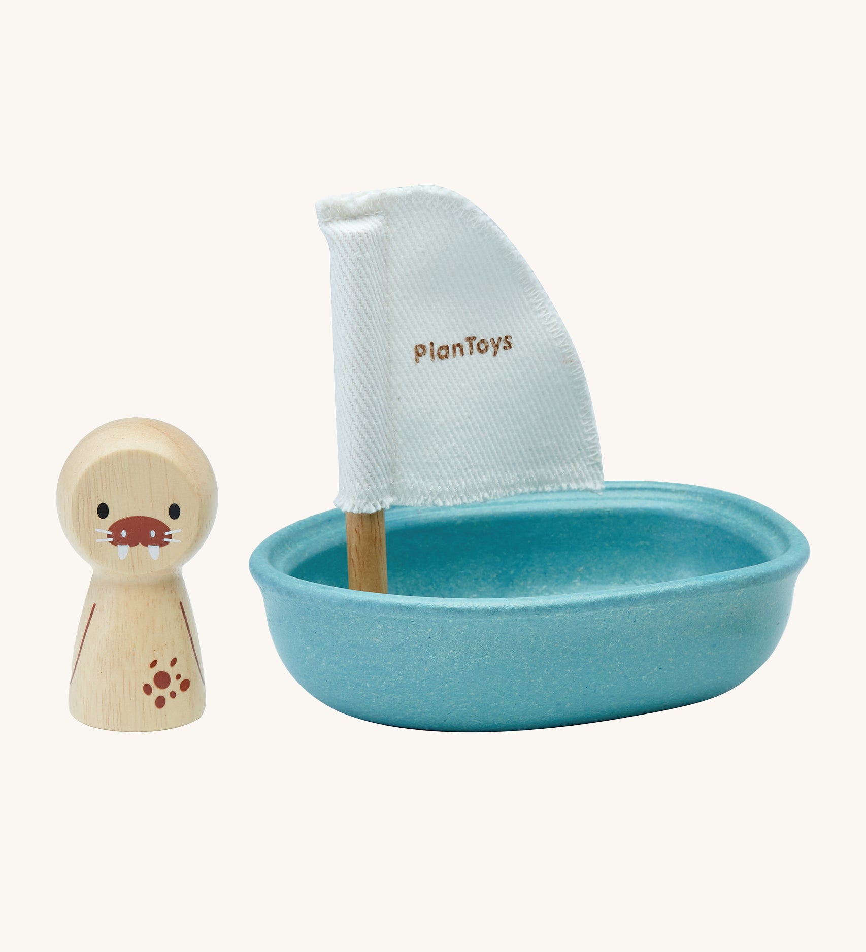 PlanToys children's wooden walrus peg doll figure is next to a blue wooden sailing boat bath toy with a white sail, and is on a cream background