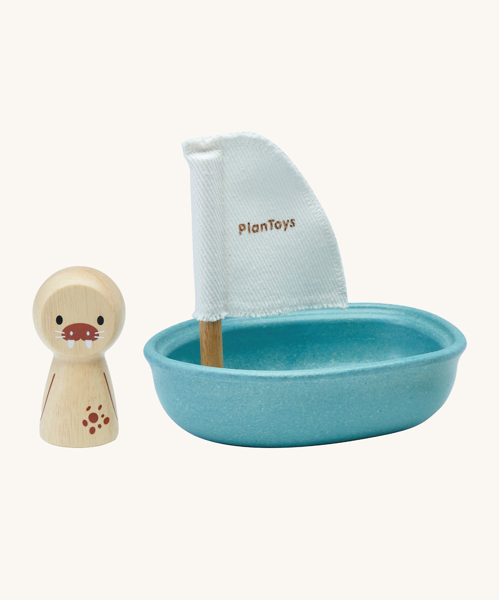 PlanToys children's wooden walrus peg doll figure is next to a blue wooden sailing boat bath toy with a white sail, and is on a cream background