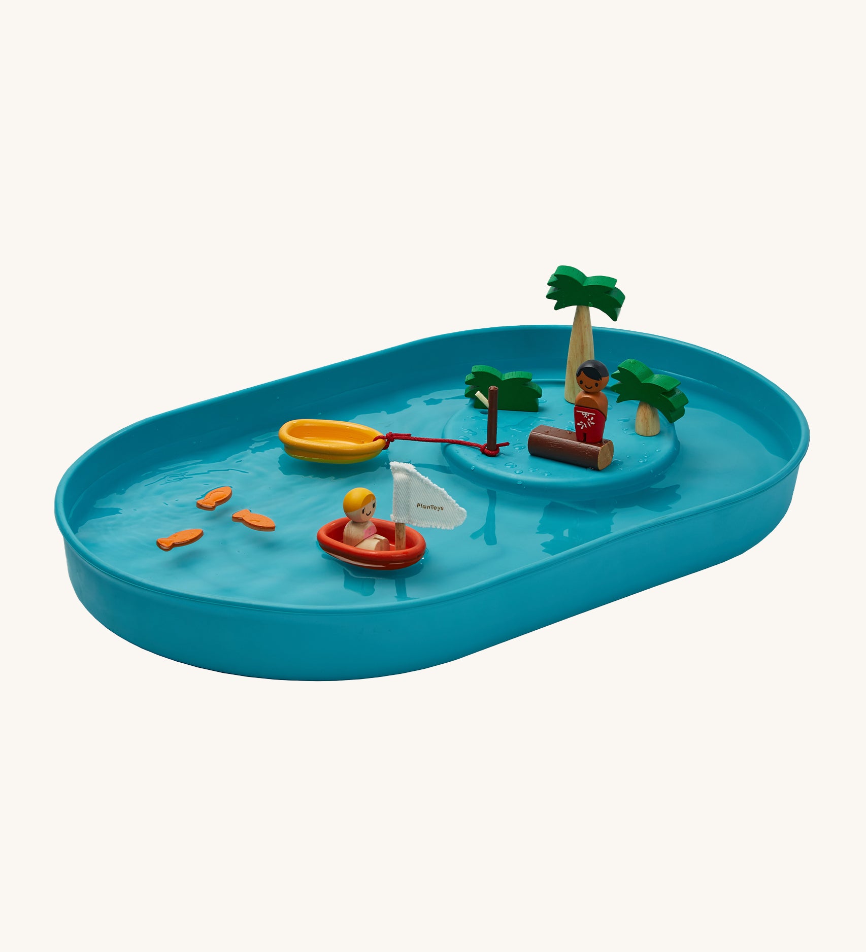 PlanToys Water Play Set is made from natural rubber and is great for sensory water play. The image shows a blue tray filled with water, with 3 fish floating on the water, a figure in a PlanToys boat, a boat tied to a brown pole and a figure stood on a wood log with palm trees to give a raised island effect. The image is on a cream background