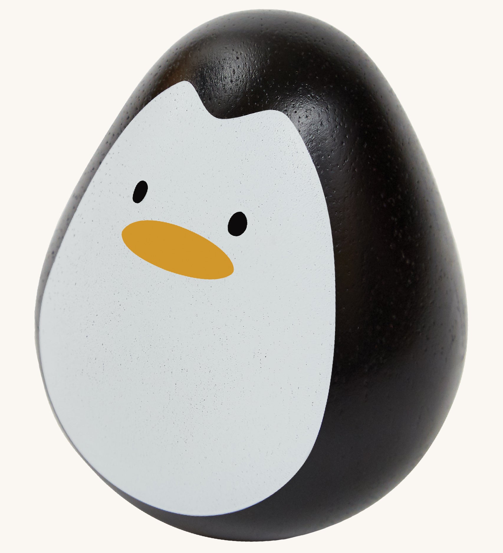 This PlanToys Penguin is a sweet wooden tumbling toy that wobbles and spins. Its size is perfect for little hands, and its smooth texture is perfect for gripping. This wobbling penguin toy is black, with a white face, black eyes and orange beak. The image is on a cream background