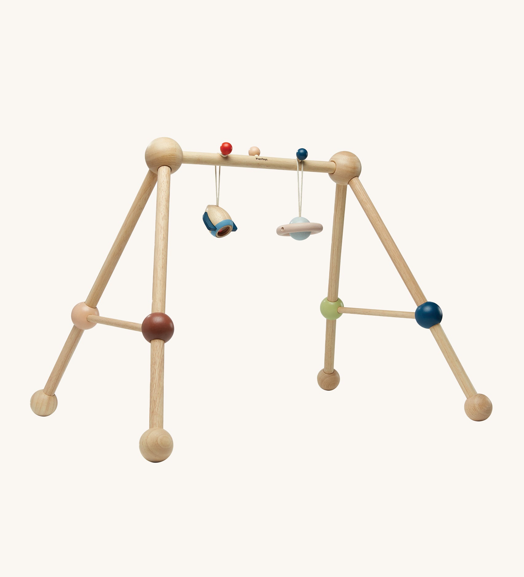 The PlanToys Play Gym Orchard is a fun, sensory baby gym made from wood. This set includes a rocket and a planet toy attached to the top of the baby gym using a red and a blue peg. This is a side view image on a cream background.