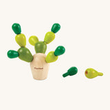 The PlanToys Mini Balancing Cactus with the green cactus pegs balanced carefully in the natural wooden cactus block, with two green cactus pegs to the right side of the cactus, on a cream background