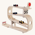 PlanToys Ramp Racer is a wooden car multi-level track with 3 cars, which flip from one track to another. There is a red sign with a circle on the top track, a checkered block on the second and last tack, and a red stop section at the bottom to stop the cars from rolling away. The image is on a cream background