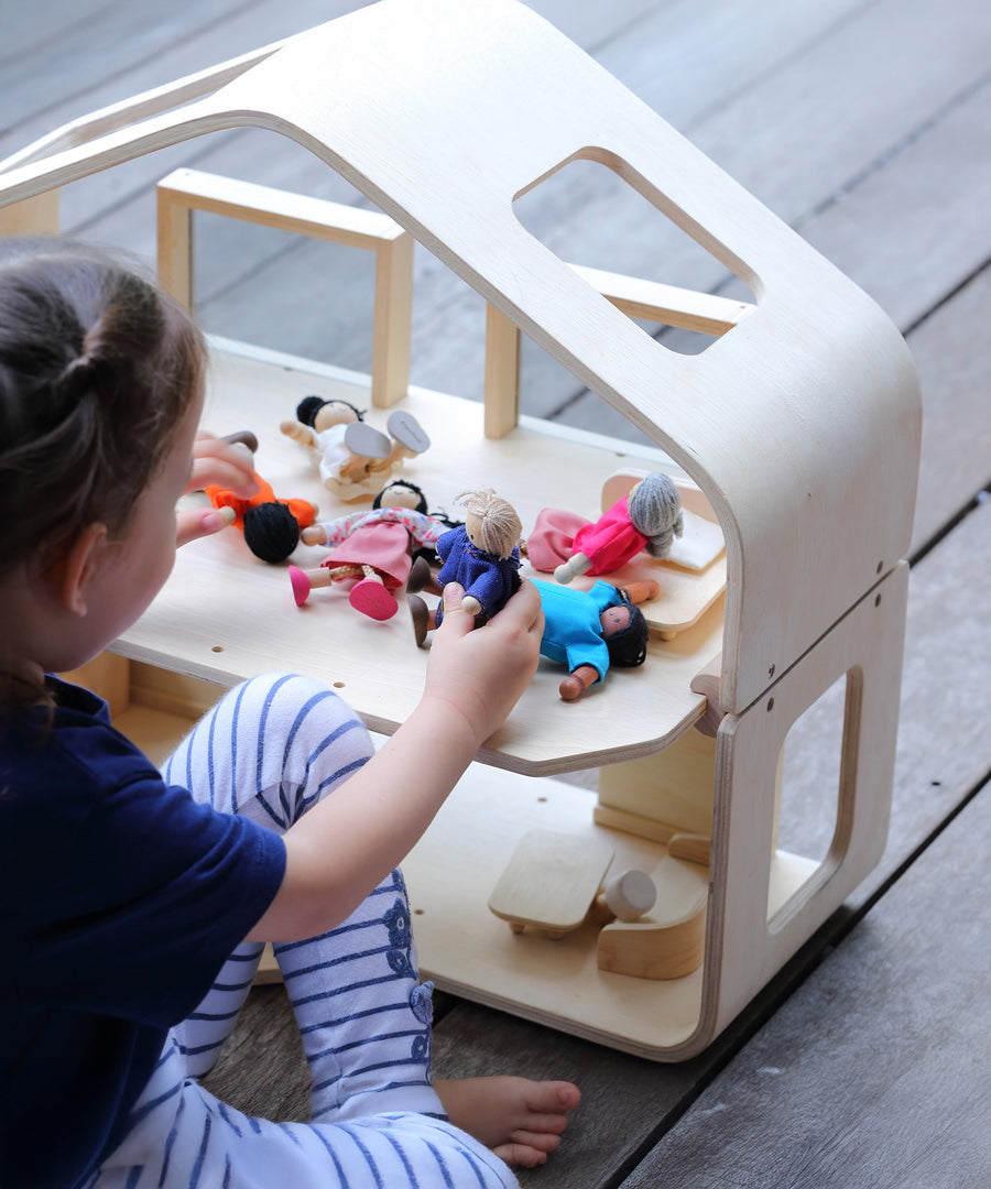 A close up of a child playing with the PlanToys Contemporary Dolls House. There are wooden dolls and wooden furniture inside. 