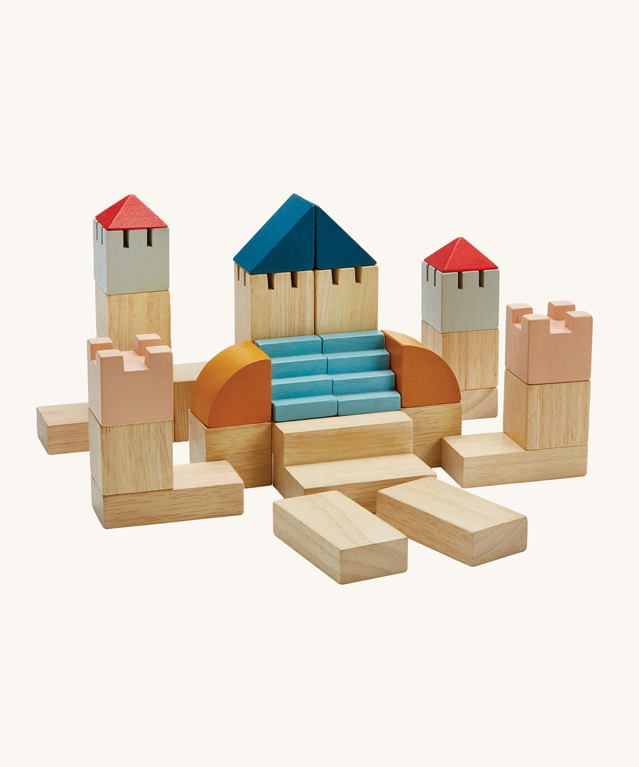 PlanToys Creative Blocks in the colourwave Orchard, are a set of building blocks in various shapes and colours which include natural coloured blocks, coral pink, blue, red, grey and mustard. The image is on a cream background