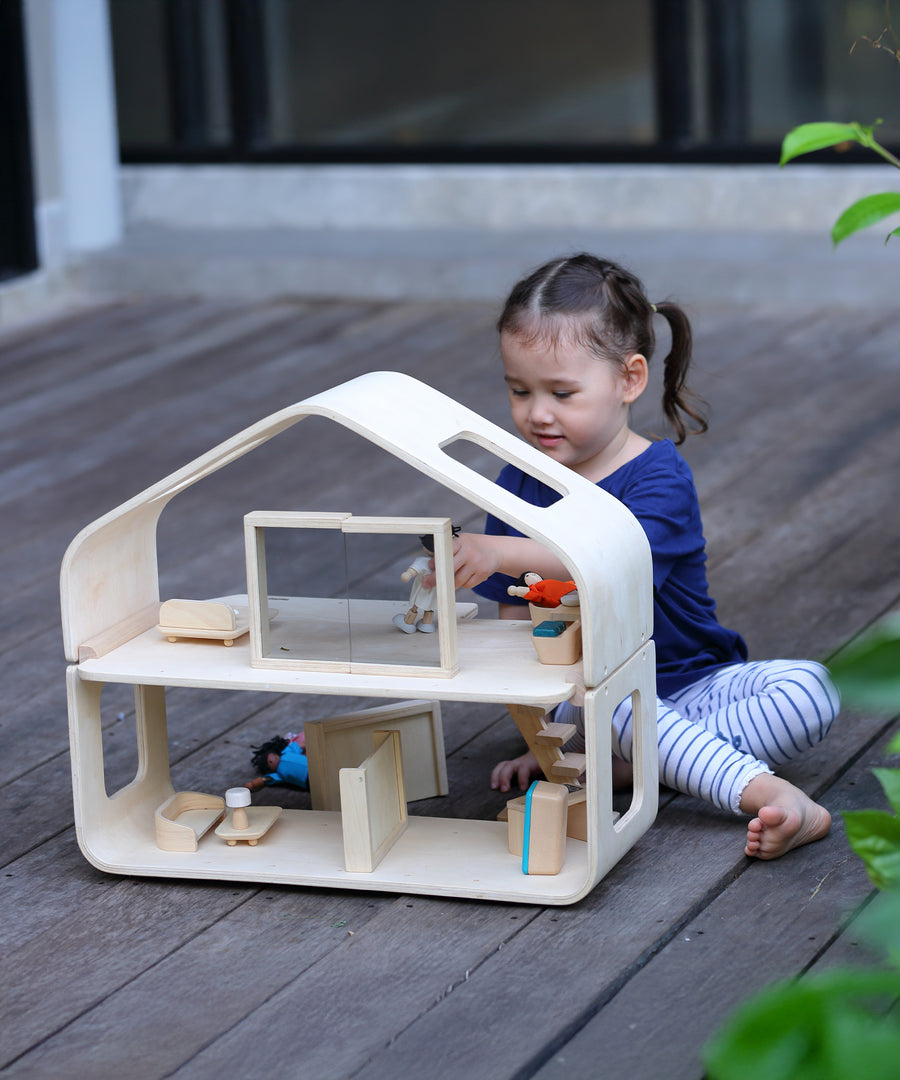 A child playing with the PlanToys Contemporary Dolls House. There are wooden dolls and wooden furniture inside. 