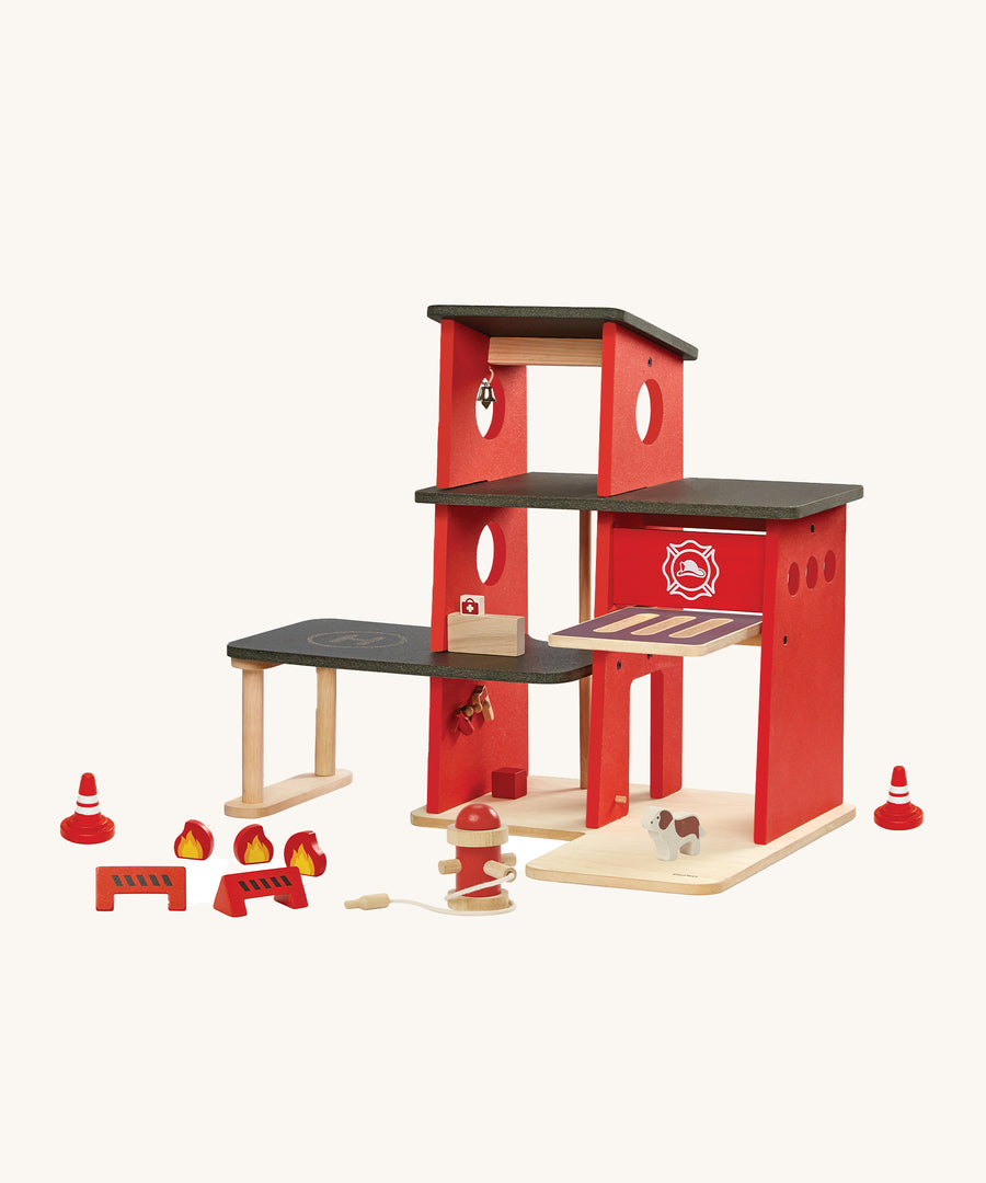 The PlanToys Fire Station with little wooden figures around the bottom of the fire station, on a cream background