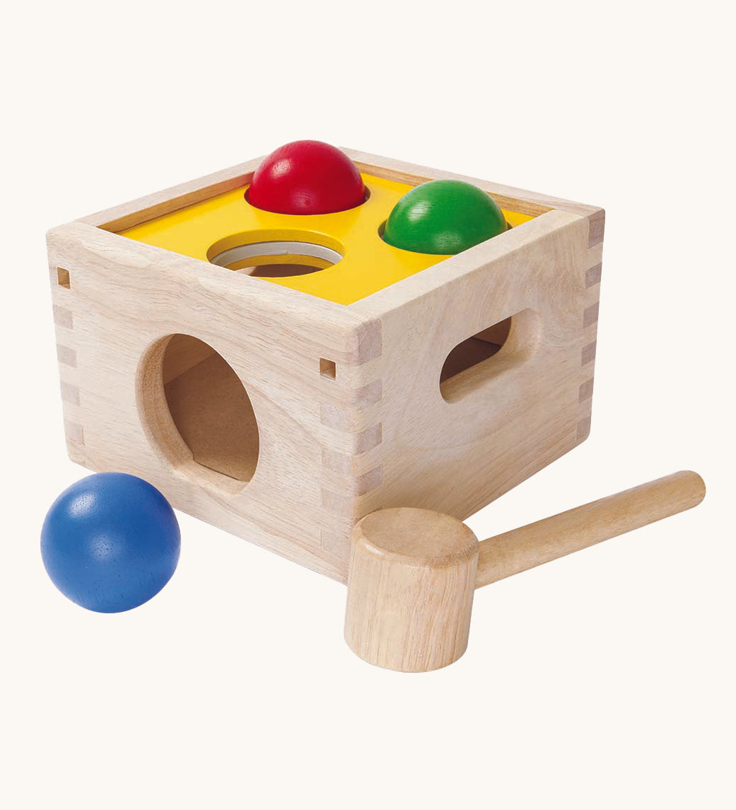 This PlanToys Punch and Drop game is a classic wooden pounding toy that babies and toddlers love – use the hammer to gently whack the three coloured balls through the holes in the wooden box and watch as they roll out. The ball colours are blue, red and green, and the top of the pounding box is yellow. The image is on a cream background