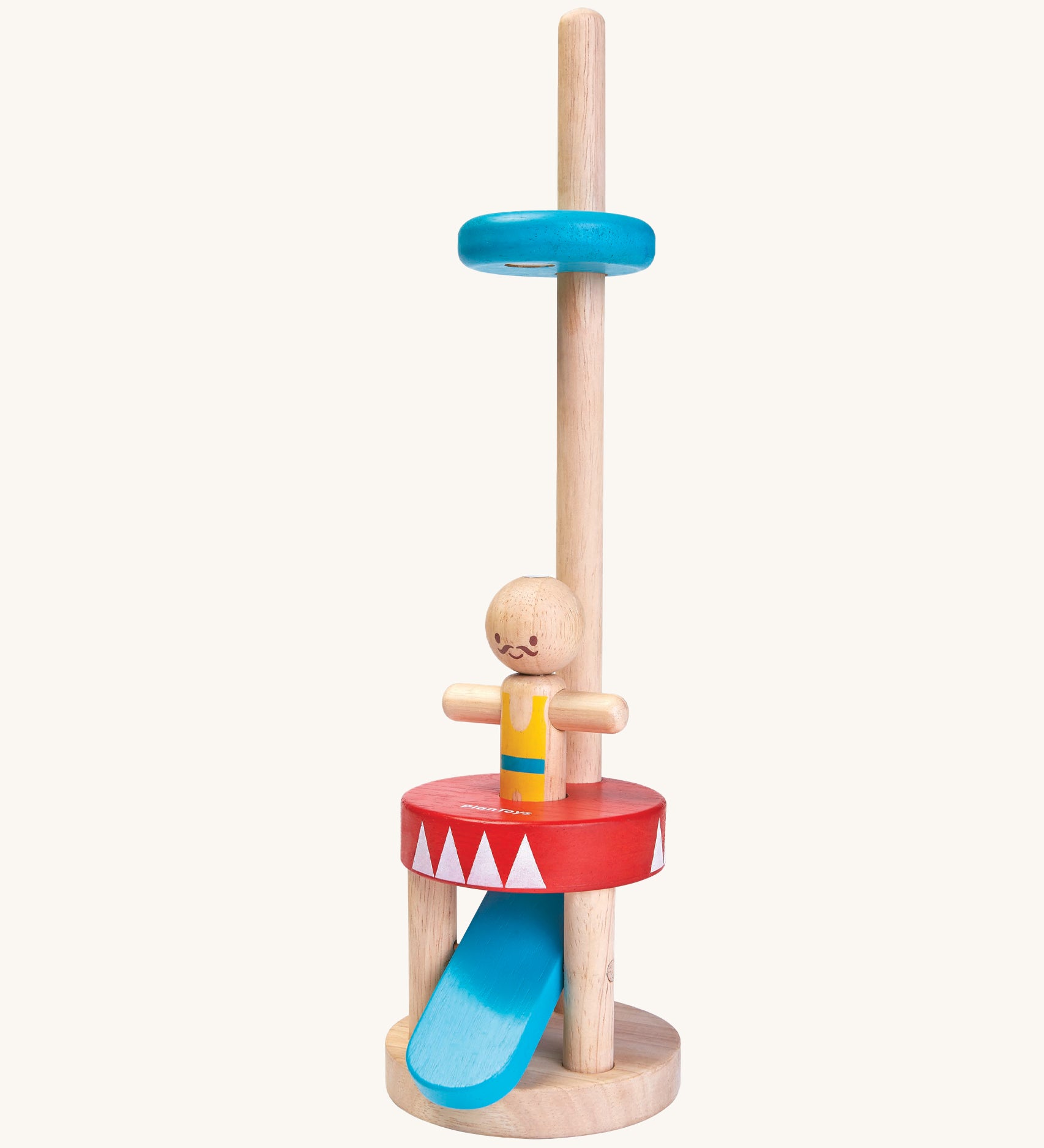 The PlanToys Jumping Acrobat is a magical toy which consists of a wooden peg acrobat with a yellow and blue top, a smiling face with a mustache, a red and white base, a blue push pedal underneath the base, and a blue disk on a wooden pole to catch the figure when it pops up. The image is on a cream background