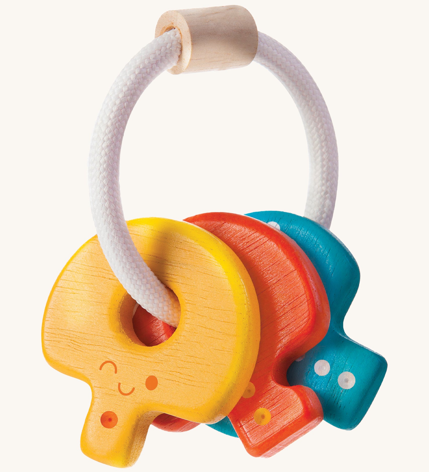 PlanToys Baby Key Rattle is a fun sensory toy for little ones. This toy is great for teething and soothing sore gums. There is a circular white rope with a wooden bead at the top. Attached to the rope are three, colourful wooden keys, all with smiling faces and dots to correspond to the key. The yellow key has one dot, the red key has two dots, and the blue key has three dots. The image is on a cream background.