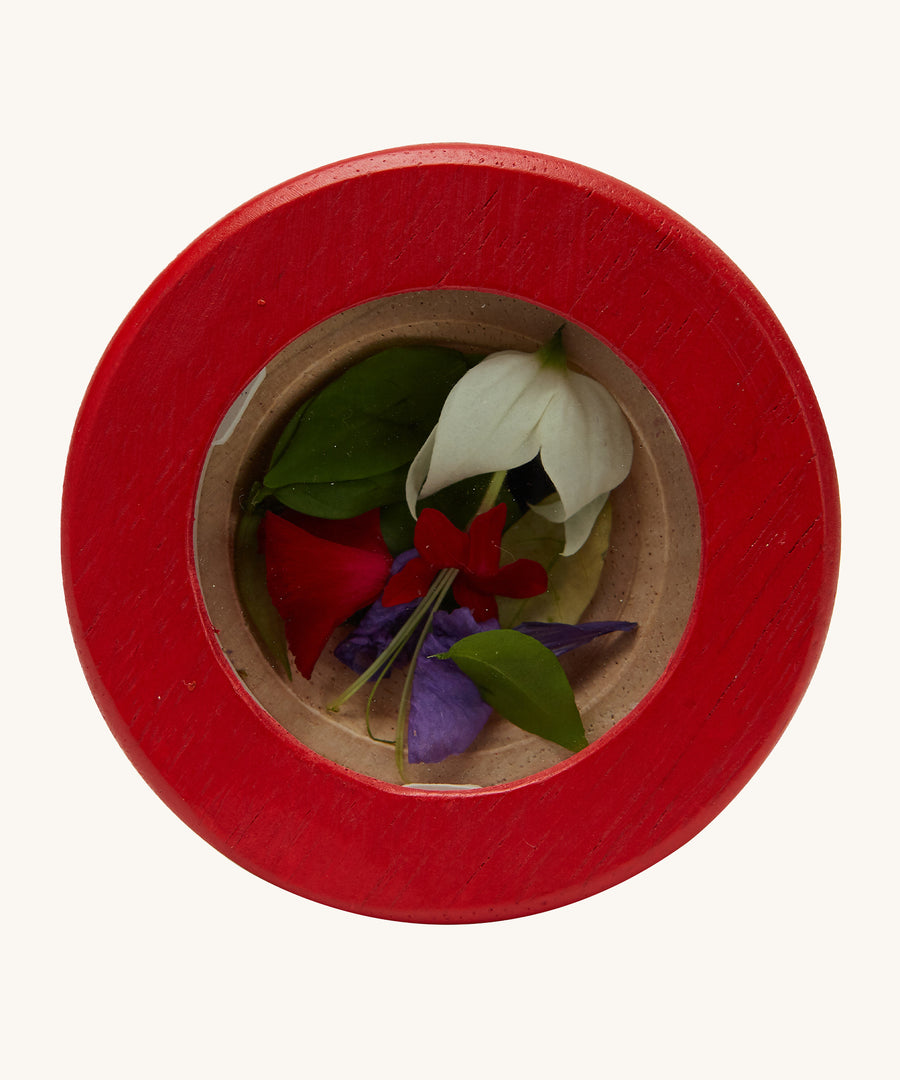 A closer look at the red lens on the PlanToys Kaleidoscope. Inside the lens are colourful red, purple and white flowers. The image is on a cream background