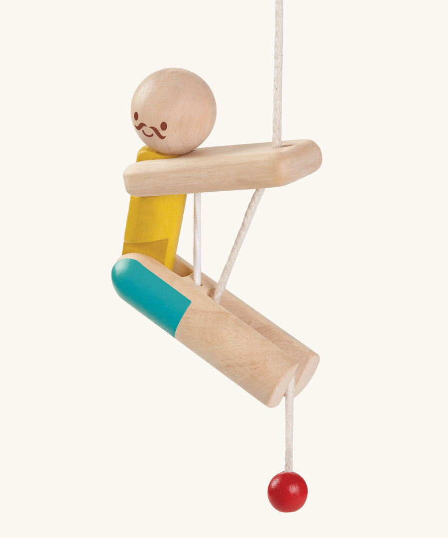 A side view of the PlanToys Rope Climbing Acrobat, showing where the white rope goes to allow the figure to climb up the rope. There is a hole in the arm section and leg section to allow the rope to pass through. The image is on a cream background