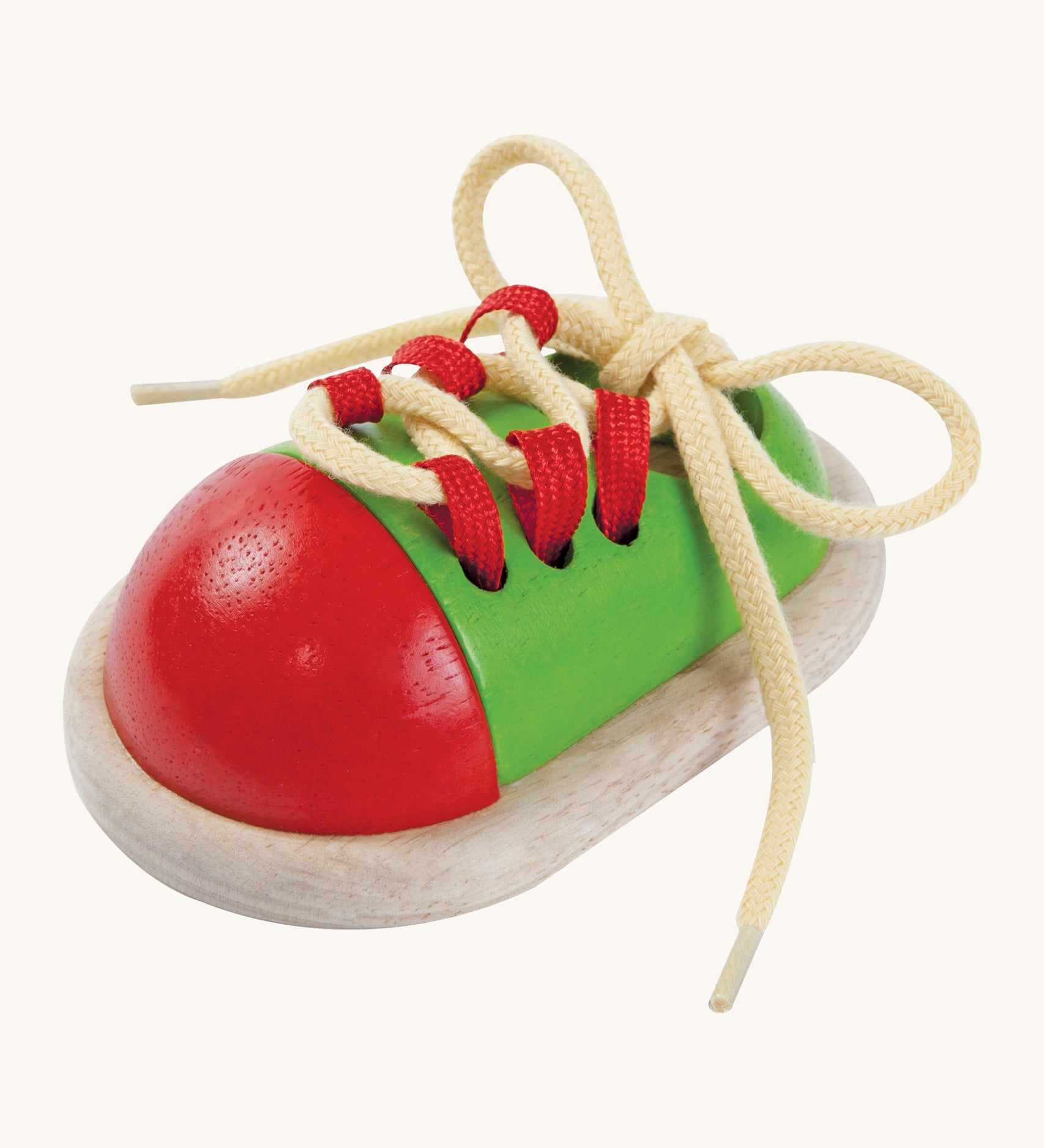 This red and green wooden shoe toy by Plan Toys is a great little toy for teaching your child how to tie their shoe laces. cream background.