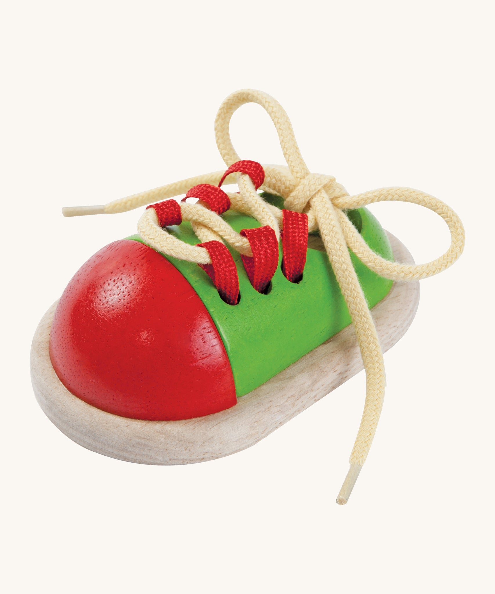 This red and green wooden shoe toy by Plan Toys is a great little toy for teaching your child how to tie their shoe laces. cream background.