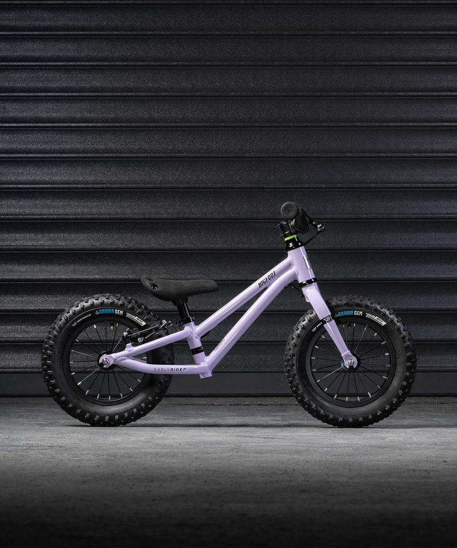 A side profile view of the Early Rider Big Foot Balance Bike - Violet Haze, on a grey textured background