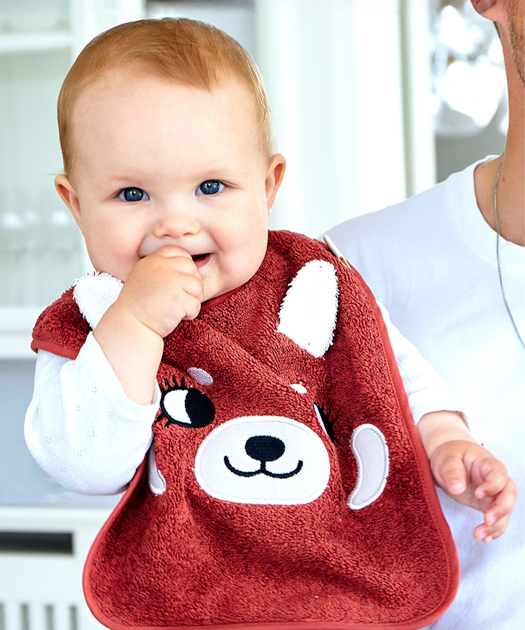 A baby being held by an adult, wearing the Roommate Organic Cotton Baby Bib - Red Panda