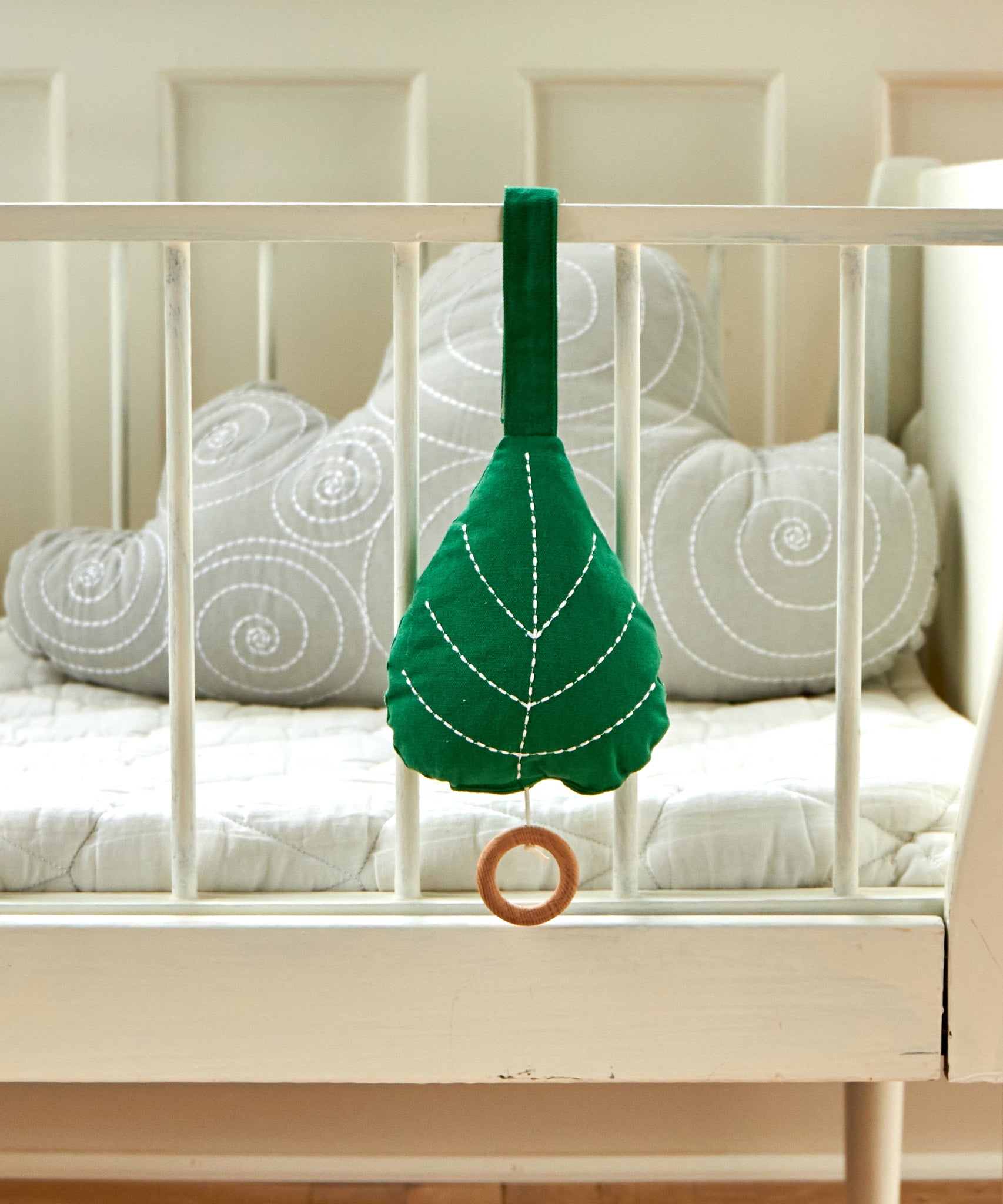 The Roommate Leaf Lullaby Music Mobile is attached to the outside of a white crib with a grey Roommate cloud cushion inside the crib