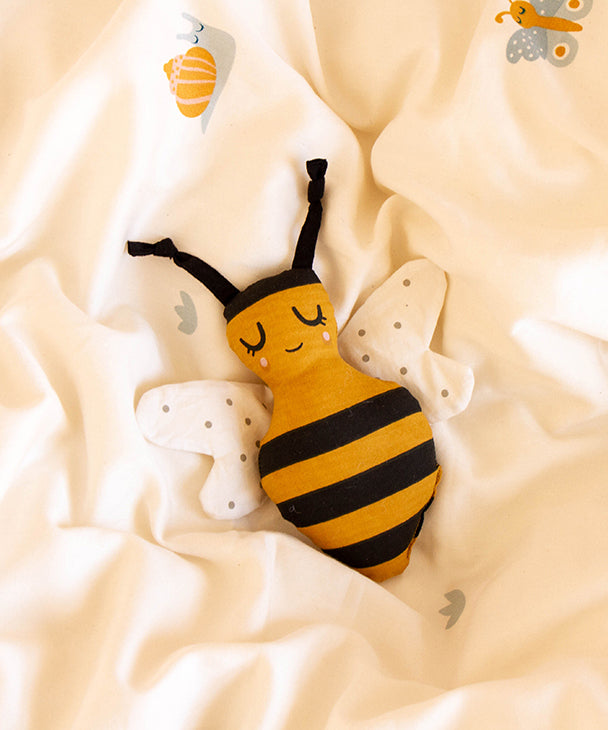 The Roommate Organic Cotton Bee Rattle, laying on a white/cream Roommate bed cover