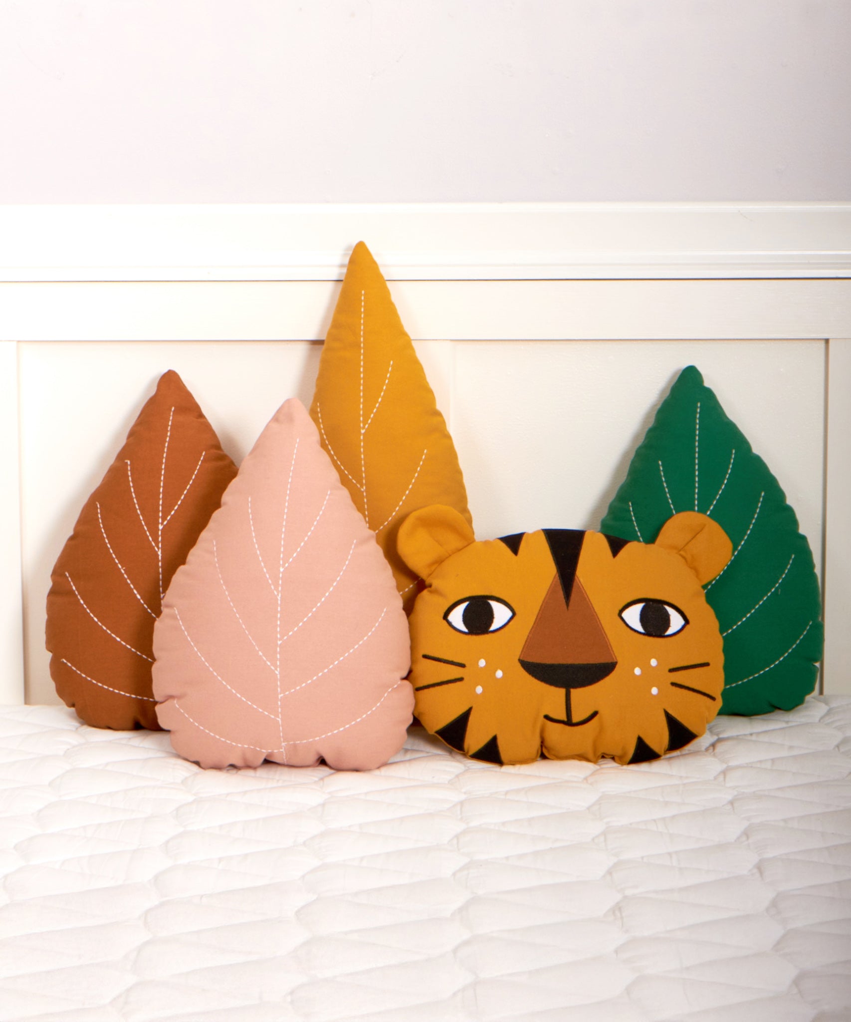 The Roommate Tiger Cushion is on a bed with Roommate Leaf cushions