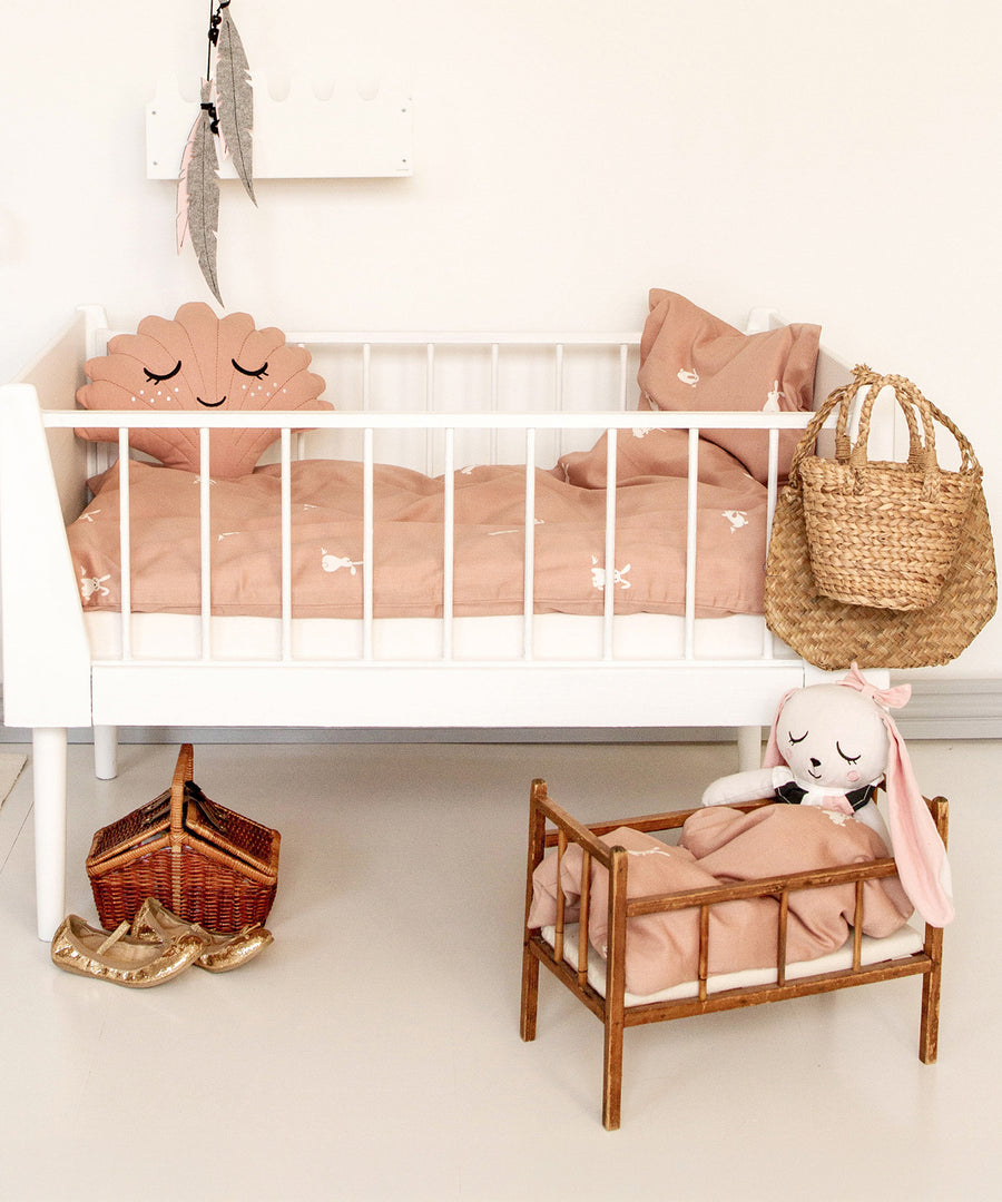 A baby's bed with the Roommate Rabbit Bedding Set is set behind a small dolls bed with the Roommate Doll Bedding Set - Rabbit inside. There is a white Roommate rabbit teddy inside the dolls bed