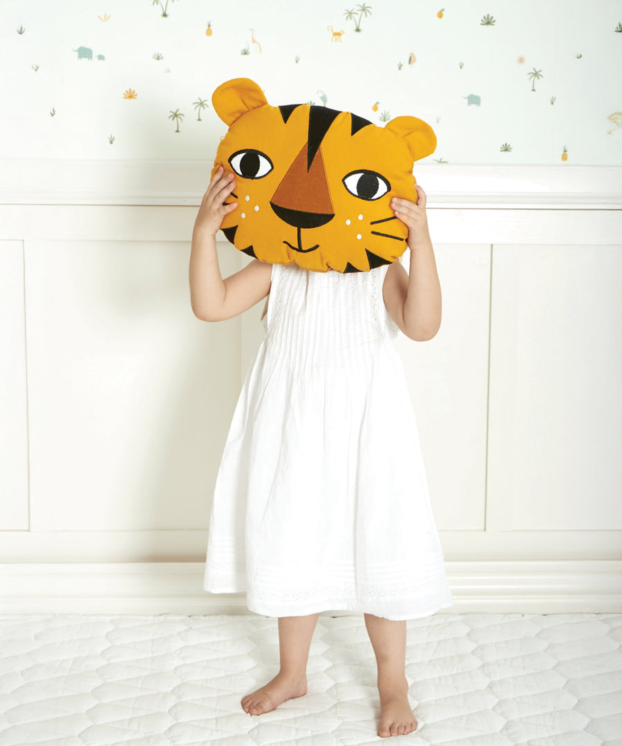 A child holding up the Roommate Tiger Cushion to their face, on a light coloured background