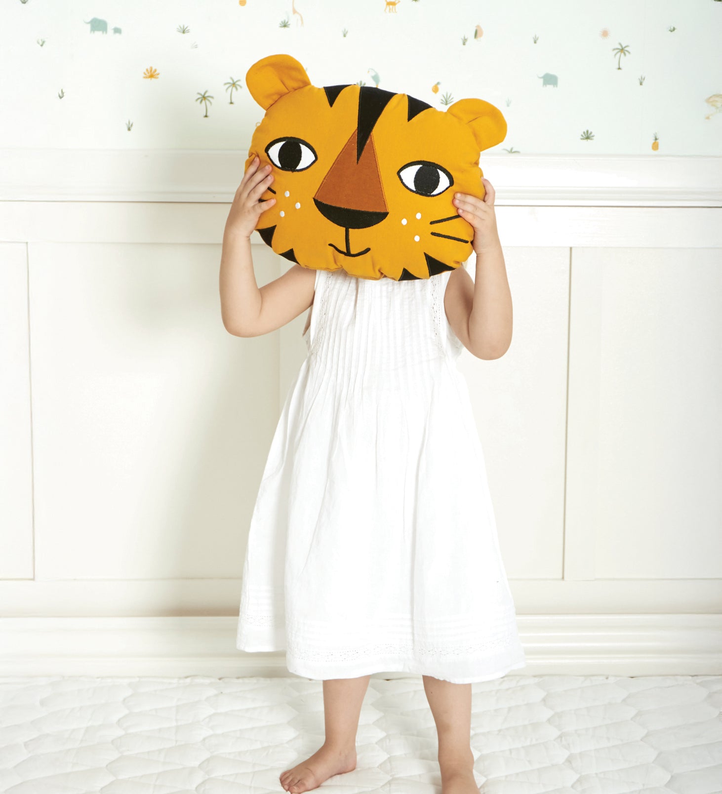 A child holding up the Roommate Tiger Cushion to their face, on a light coloured background