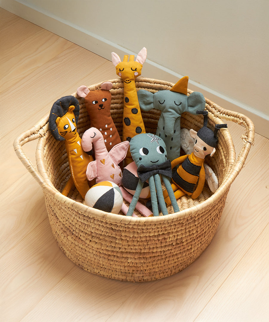 A basket of Roommate Rag Doll Organic Cotton kids toys, stood on a wooden floor