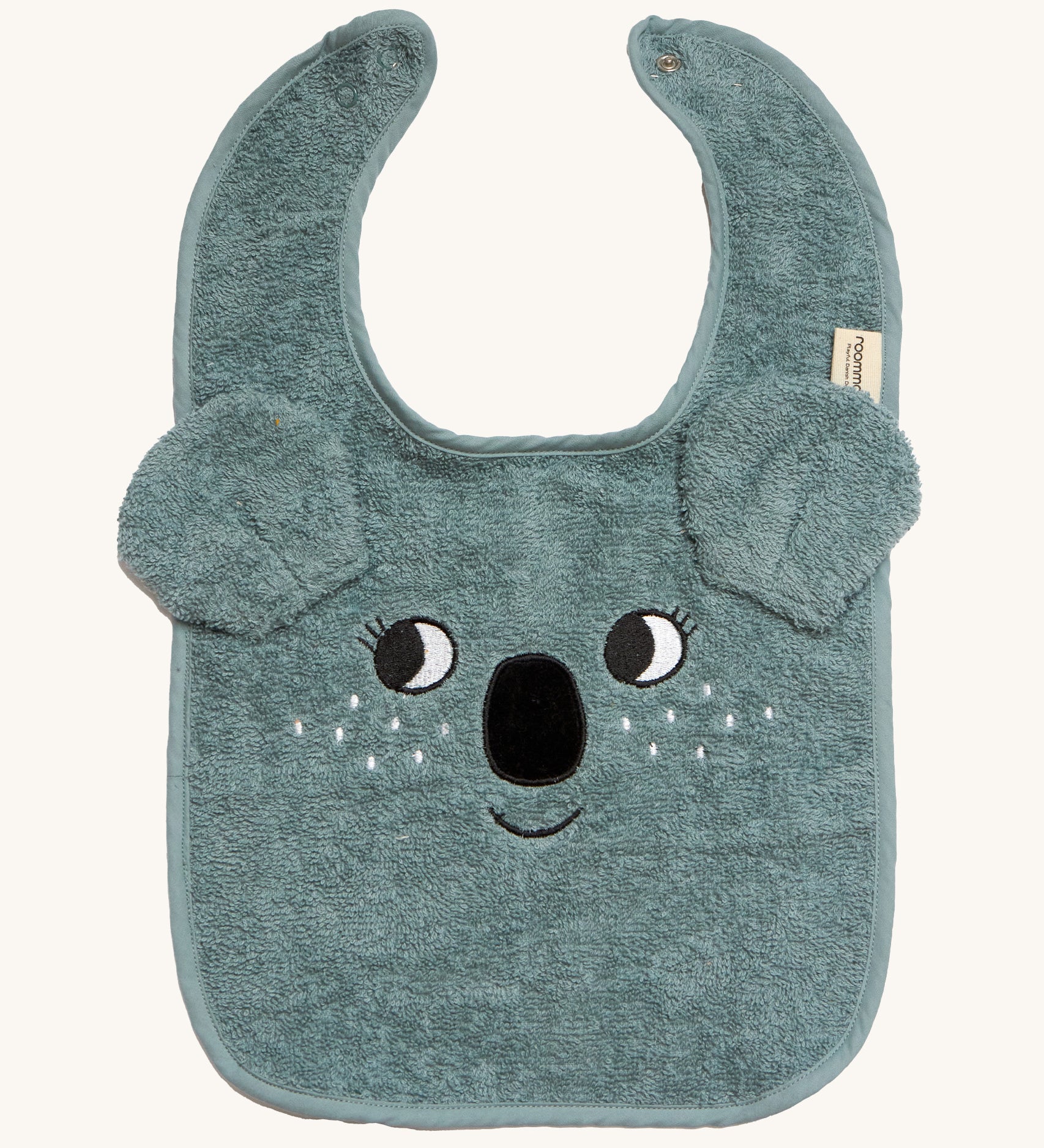 Roommate Organic Cotton Baby Bib - Koala is a soft flannel baby bib with a koala face, interactive koala ears, and metal popper fasteners to close the bib at the back of the neck. The image is on a cream background