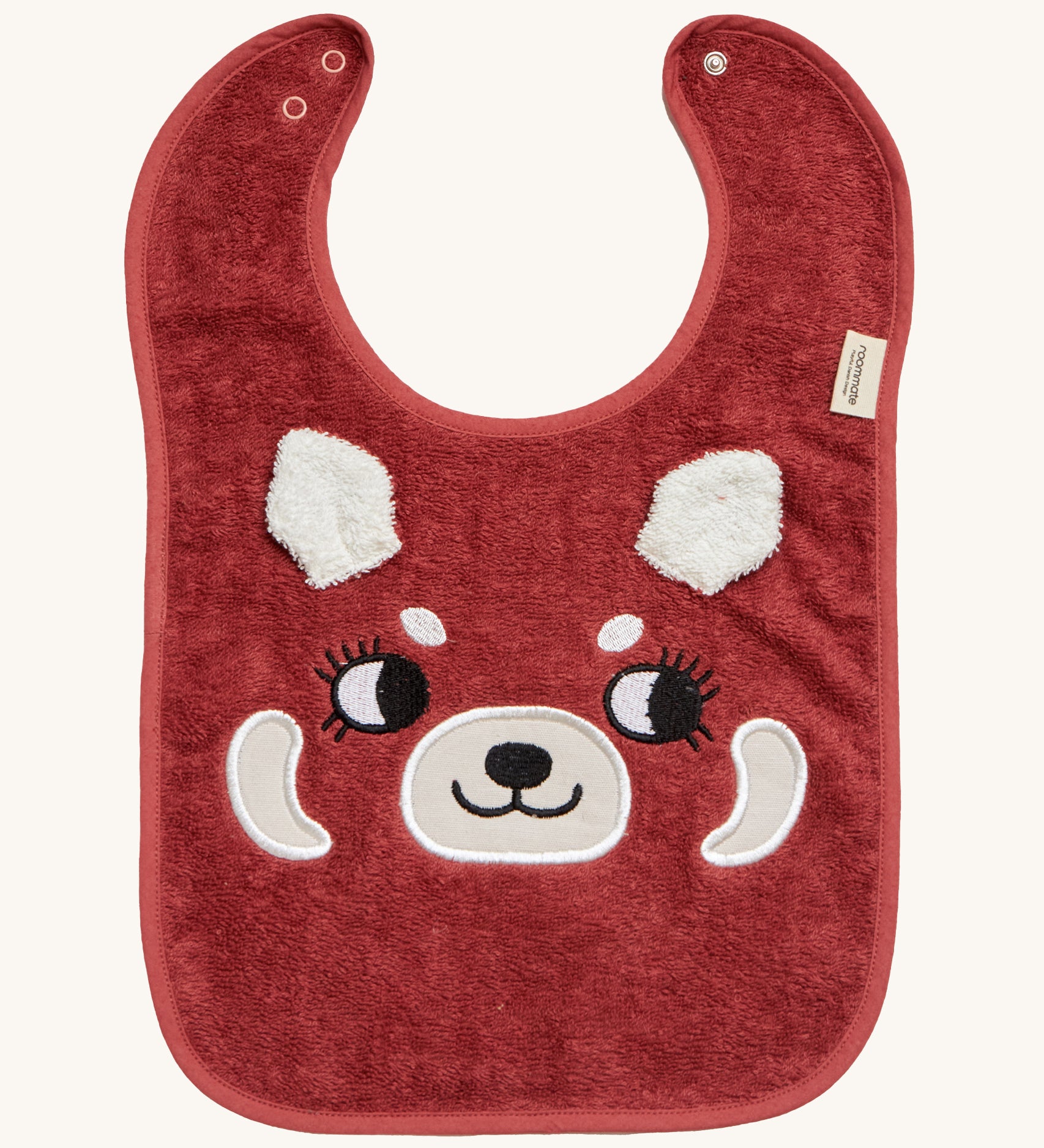 Roommate Organic Cotton Baby Bib - Red Panda, is a flannel style bib with a cute red panda face, interactive panda ears, and a metal popper fastener to close the bib behind the neck. The image is on a cream background