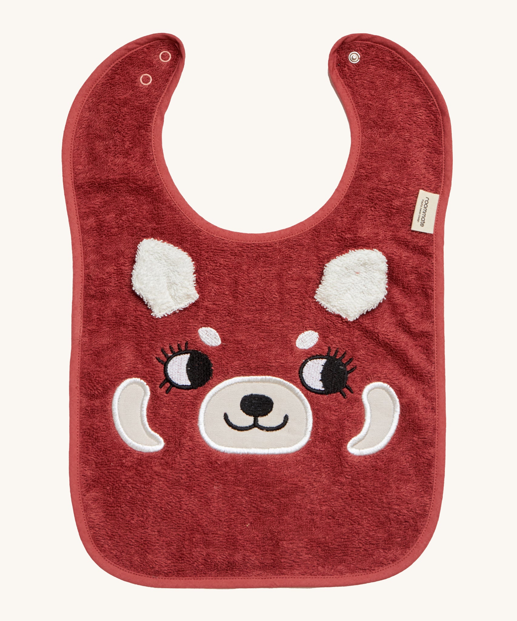 Roommate Organic Cotton Baby Bib - Red Panda, is a flannel style bib with a cute red panda face, interactive panda ears, and a metal popper fastener to close the bib behind the neck. The image is on a cream background