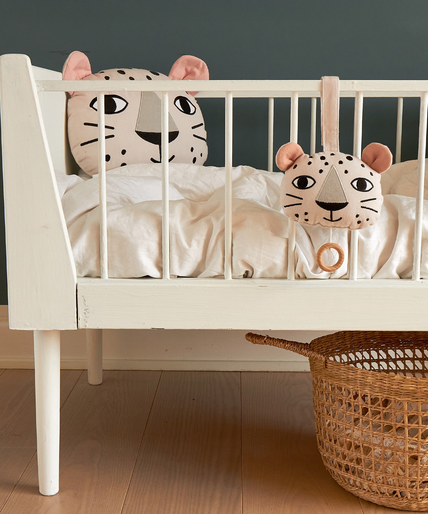 The Roommate Musical Baby Mobile - Leopard and Roommate Leopard cushion on a baby cot bed, with a basket underneath