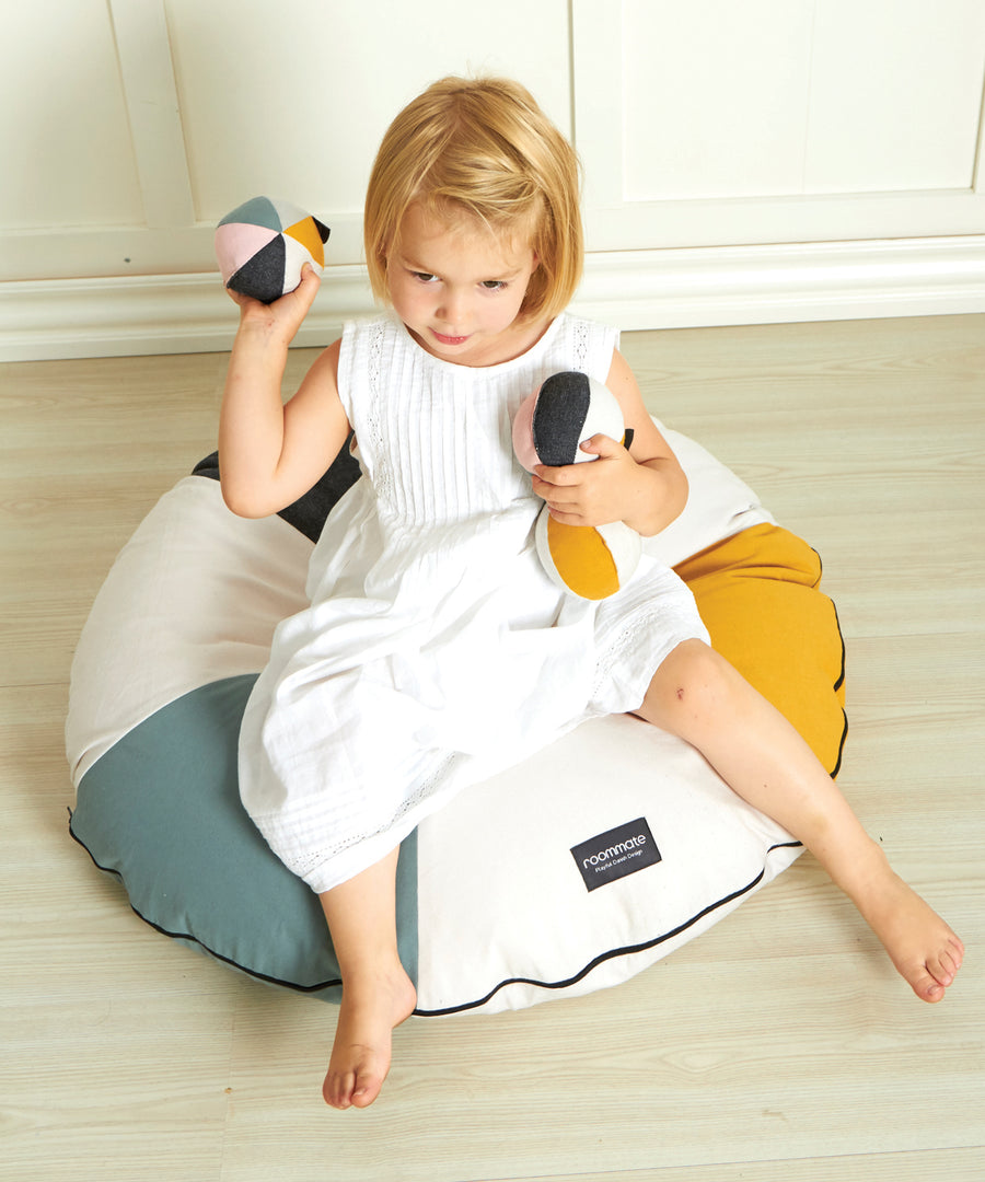 A child sat on a Roommate beanbag, playing with the Roommate Canvas Ball With Bell in Pink