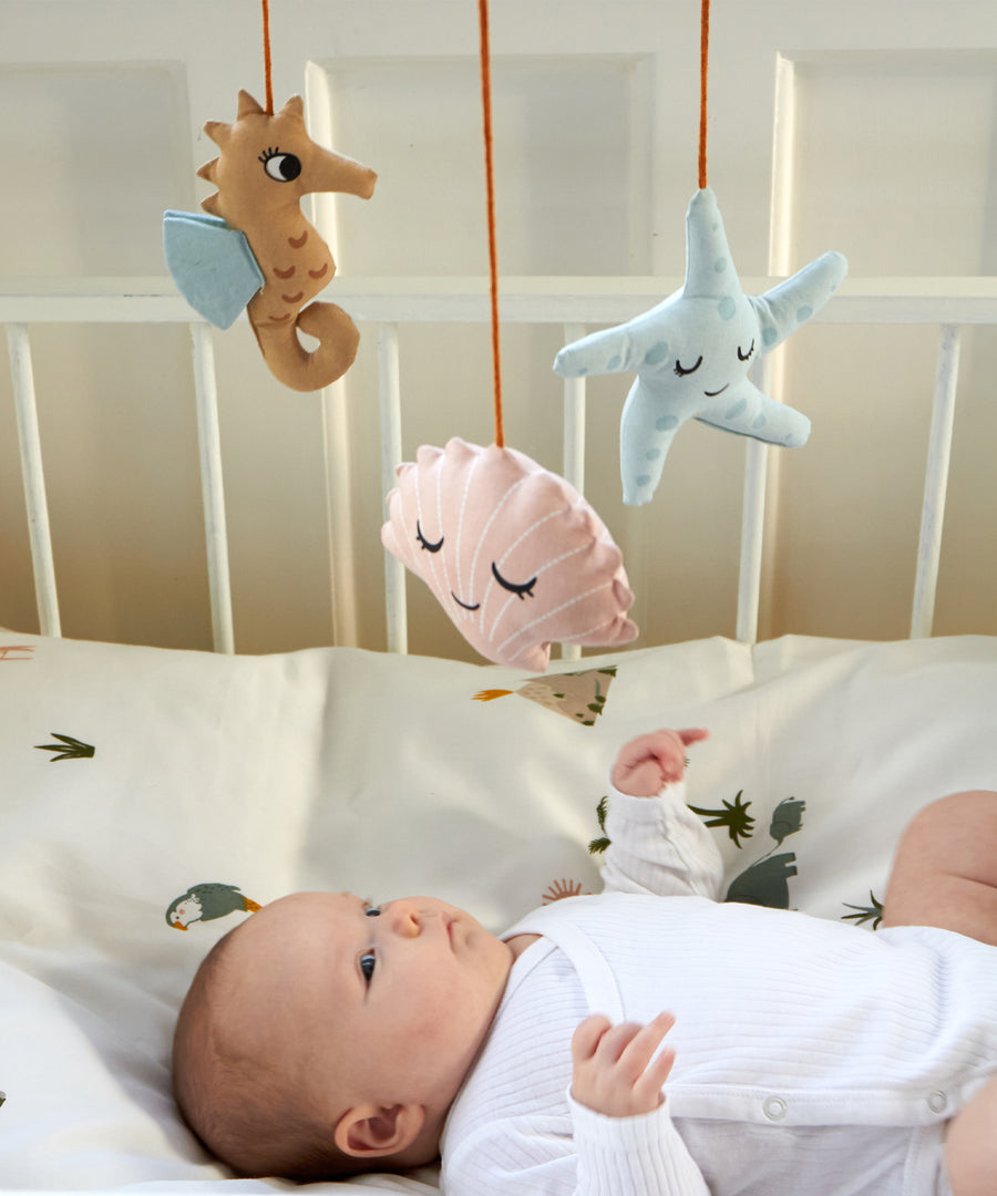 A baby laying in a crib, looking up at the Roommate Sealife Hanging Mobile