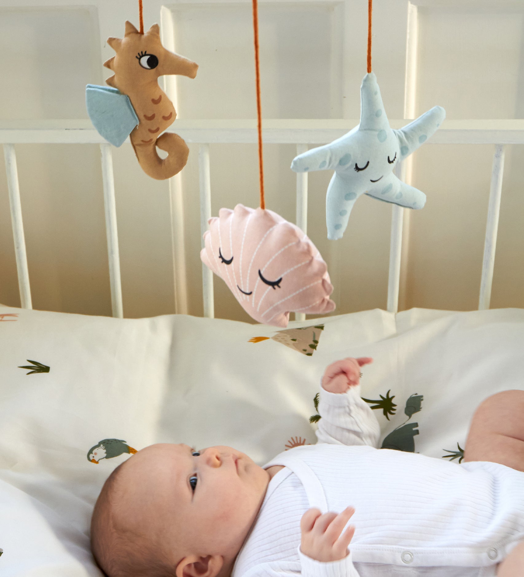 A baby laying in a crib, looking up at the Roommate Sealife Hanging Mobile