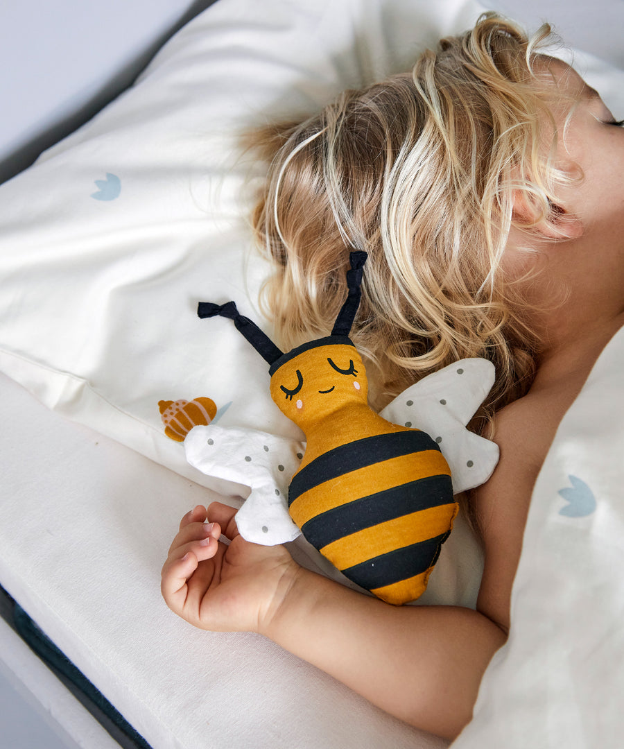 A child is sleeping with the Roommate Organic Cotton Bee Rattle next to them