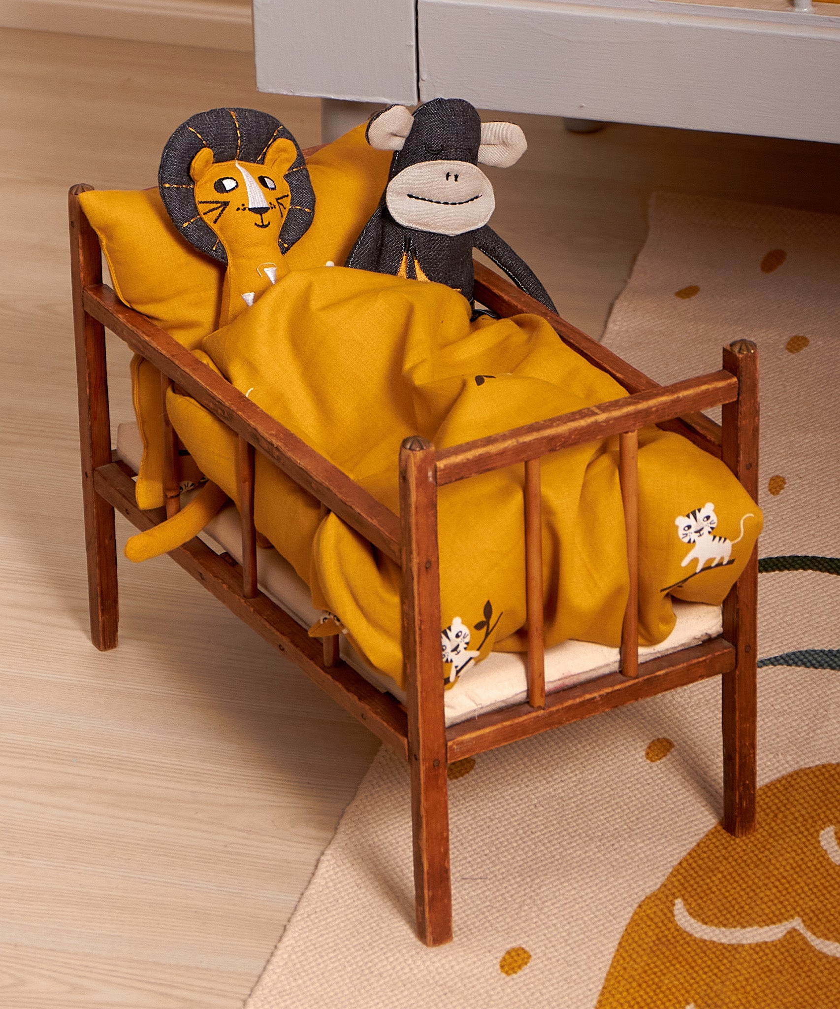 Two Roommate teddies inside a dolls bed, cuddled up under the Roommate Doll Bedding Set - Tiger