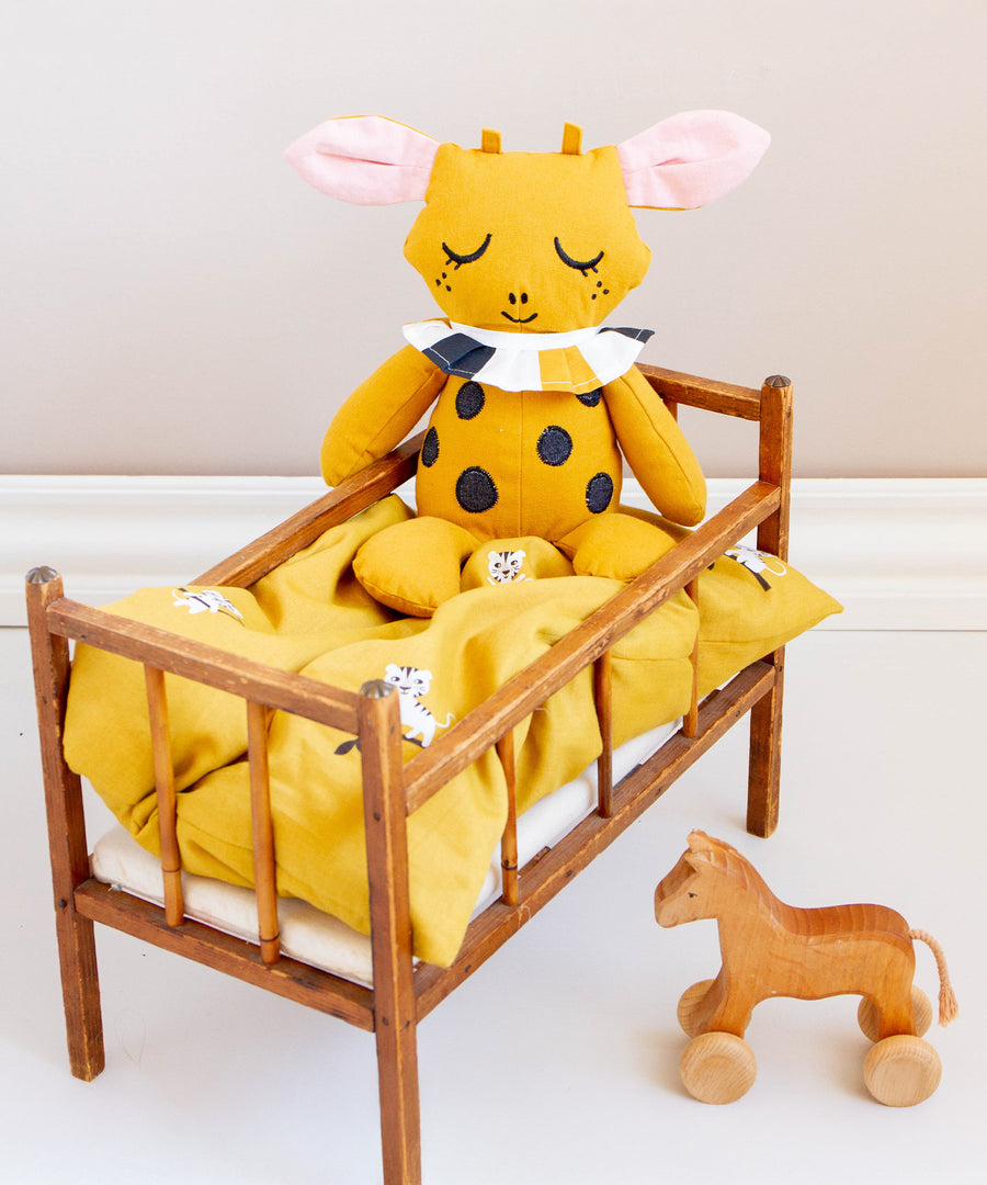 A Roommate toy sat on top of the Roommate Doll Bedding Set - Tiger, which is inside a wooden baby bed