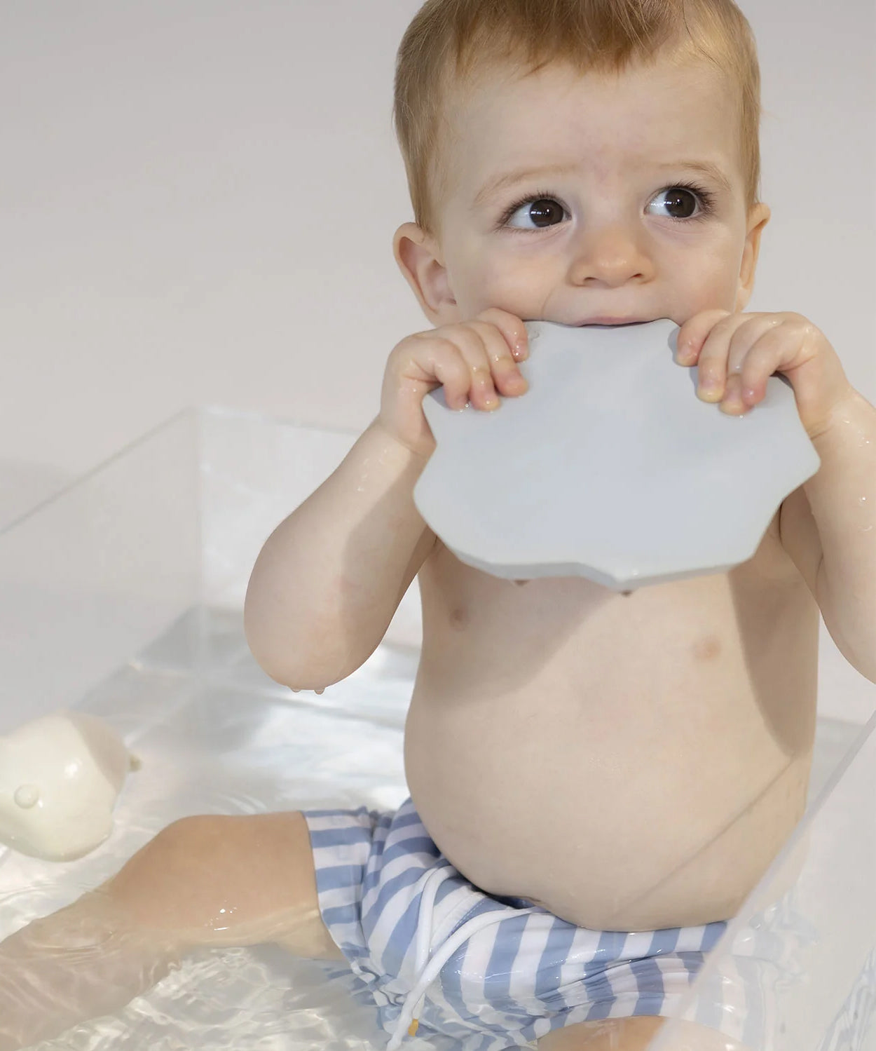 A child chewing on the base of the Oli & Carol Penguin Bath Toy Set - 100% Natural Rubber, showing how all parts of the toy can be used as a teether as well as a play toy